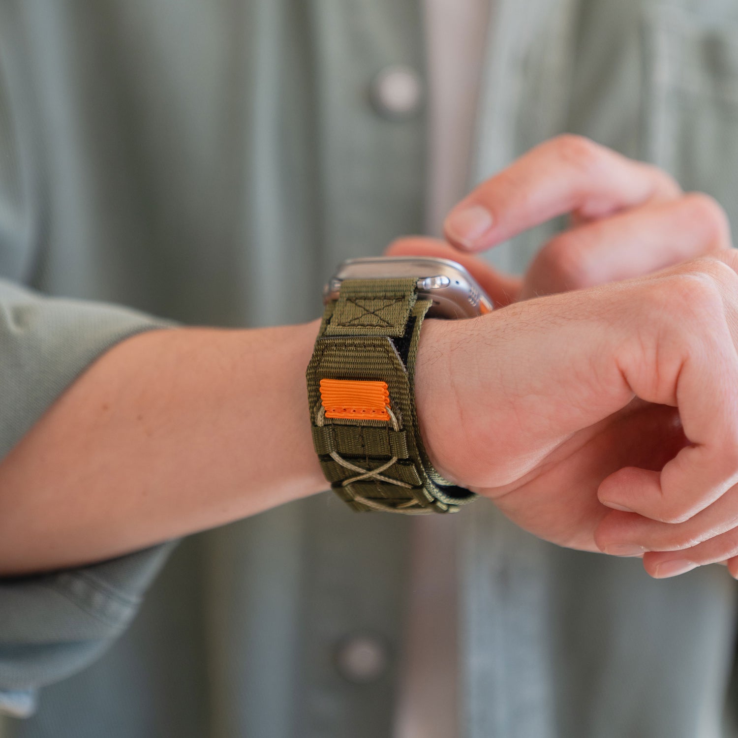 Nahaufnahme einer Person, die das arktisband Apple Watch Outdoor Armband "Forge" mit grünem Stoffband trägt und den Bildschirm der Smartwatch berührt.