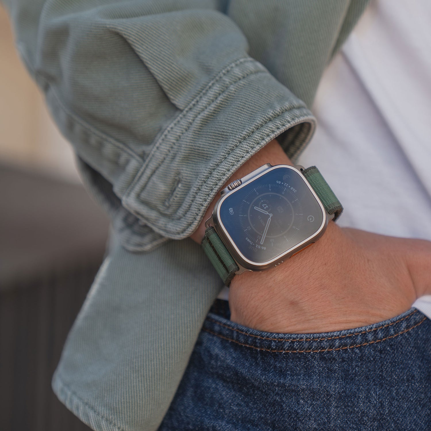 Eine Person in grüner Jacke trägt das arktisband Apple Watch Armband "CoreX" von arktisband mit grünem Armband und Fallschirm-Verschluss, die Hand in der Jeanstasche verstaut.