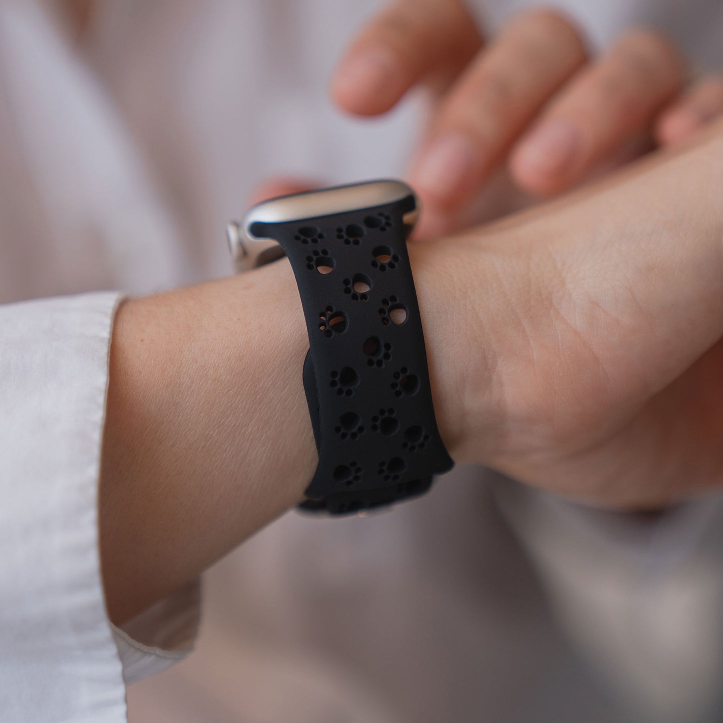 Eine Person trägt ein Arktisband Apple Watch Silikonarmband "Paw" mit schwarzer Farbe und kleinen Pfoten-Design-Ausschnitten.