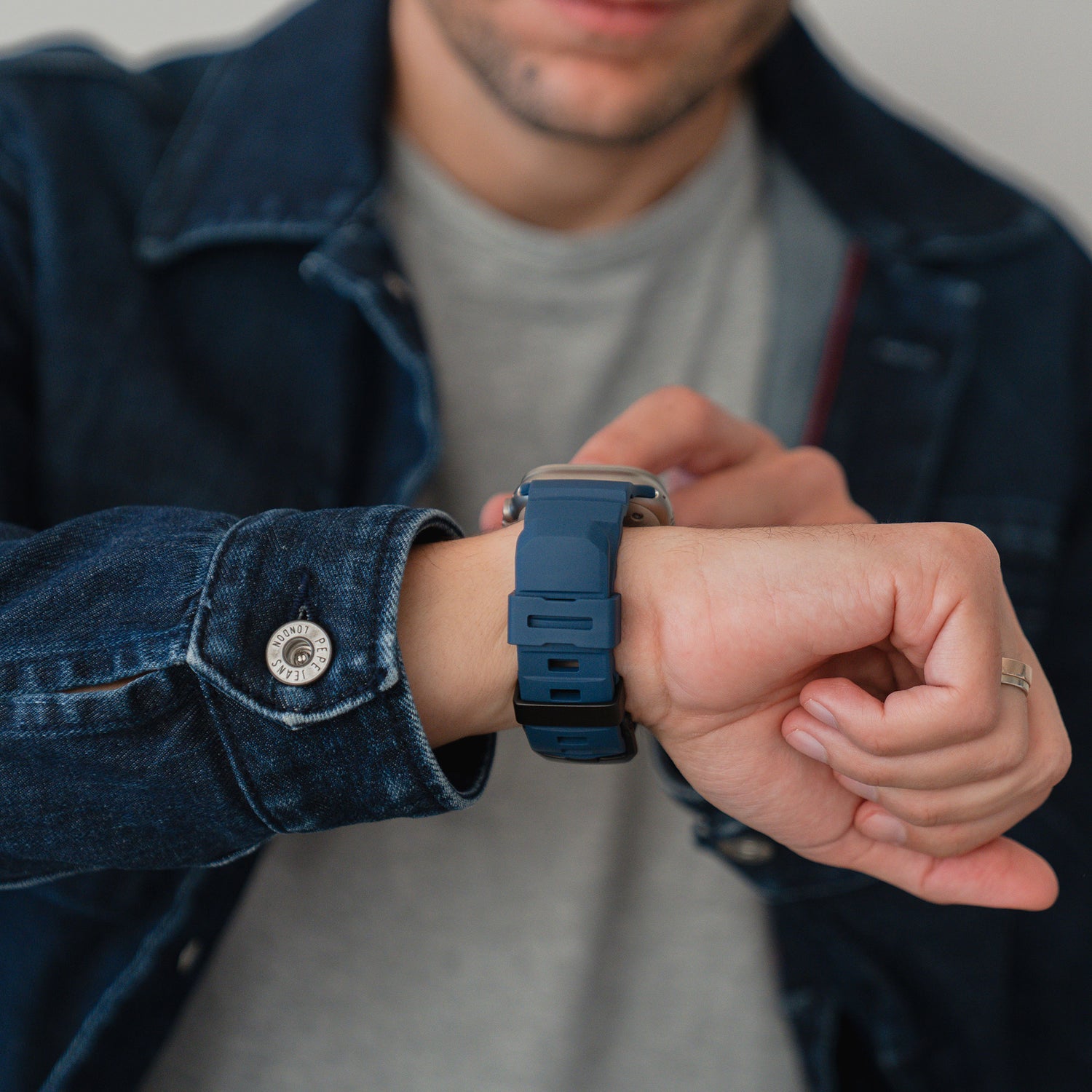 Ein Mann in Jeansjacke passt das arktisband Apple Watch Armband "Flux" mit FKM-Band und Edelstahlschließe an seinem Handgelenk an.