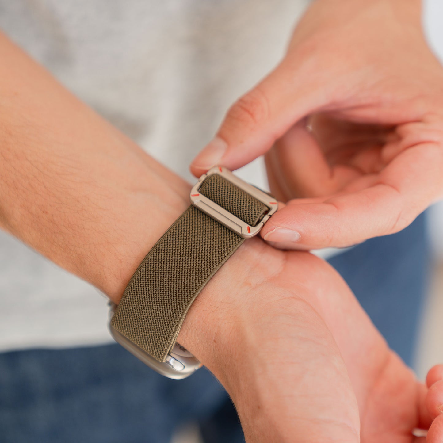 Eine Person legt sich ein Arktisband Apple Watch Nylonarmband "FlexOne" aus khakifarbenem Stoff um ihr Handgelenk.