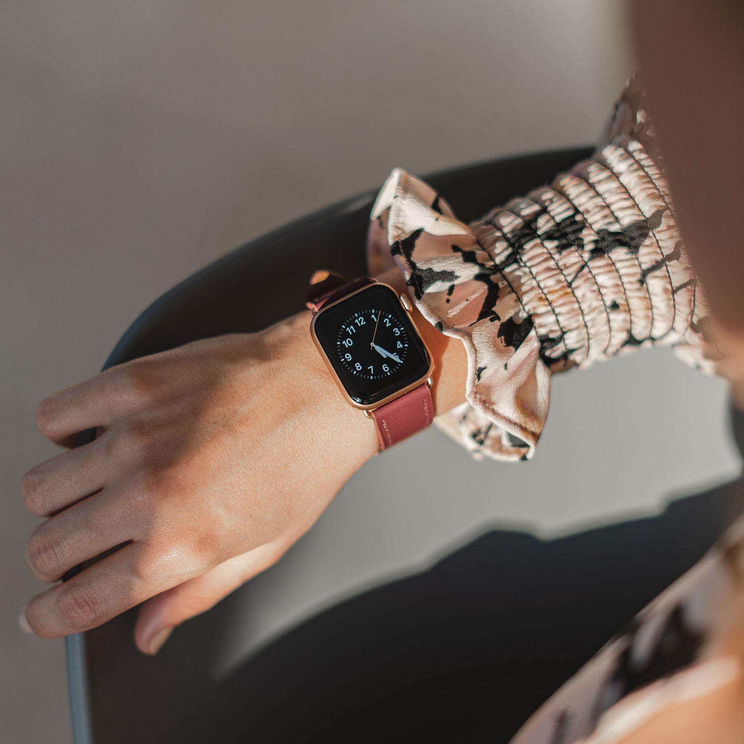 Jemand, der das arktisband Apple Watch Lederarmband "Premium" in Braun trägt, gepaart mit einem gemusterten langärmeligen Oberteil, stützt seinen Arm auf einen Stuhl.