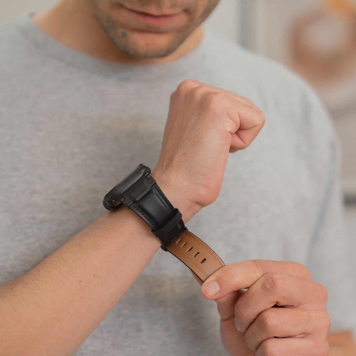 Ein Mann in einem grauen Hemd legt ein Arktisband Apple Watch Ultra Lederarmband "Delta" mit einem braunen Lederarmband an.