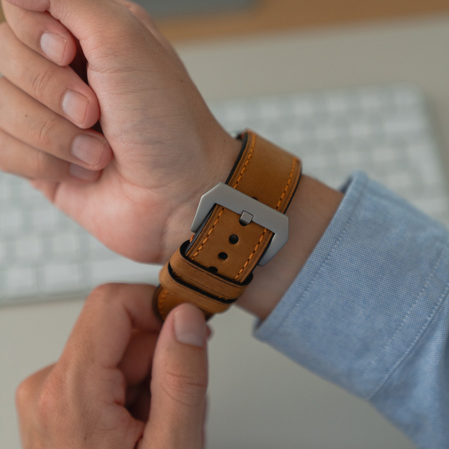 Jemand befestigt das Arktisband Apple Watch Ultra PALERMO GRANDE Lederarmband mit einer 316L-Edelstahlschließe an seinem Handgelenk neben einer Computertastatur.