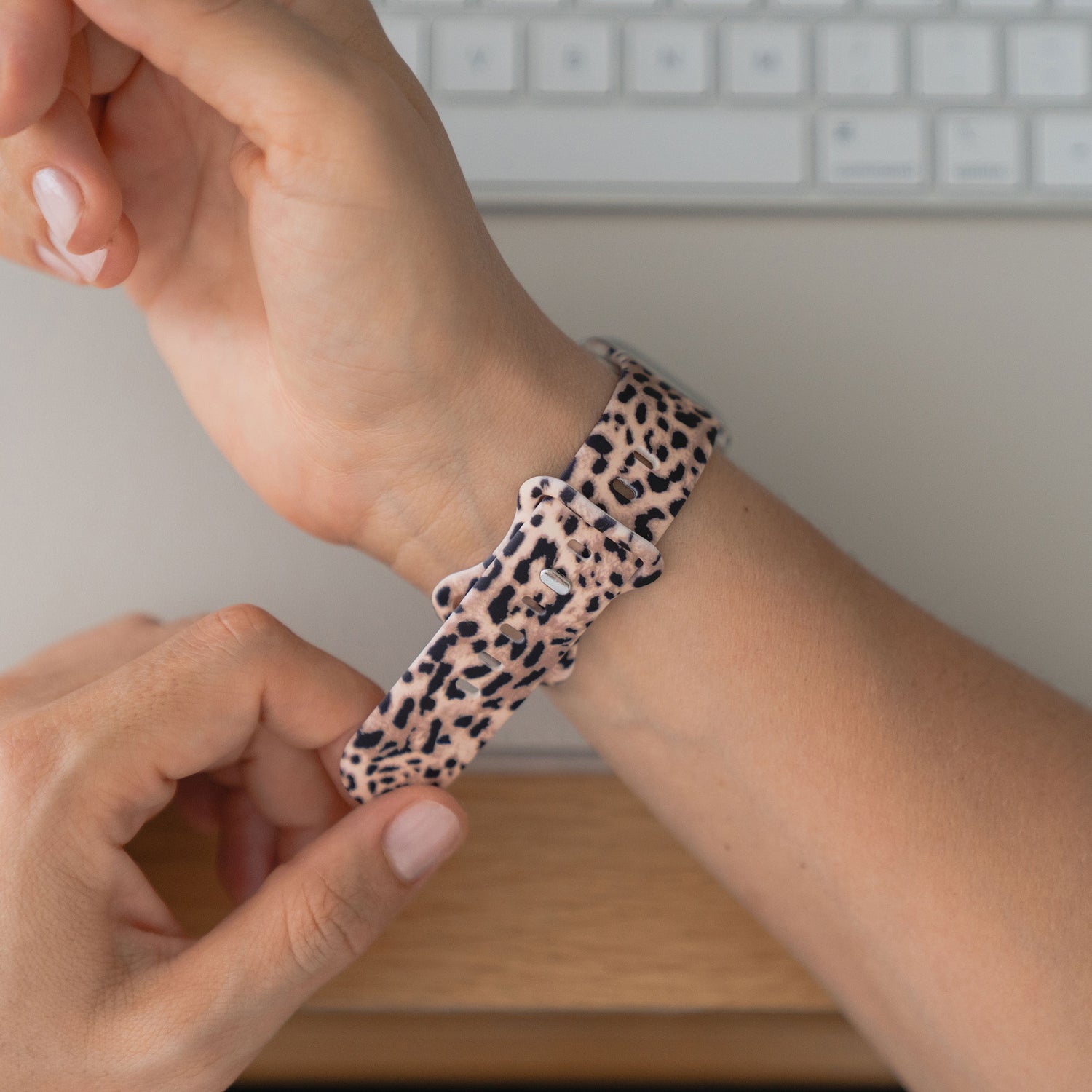 Eine Hand verstellt das arktisband Leopard Apple Watch Armband von arktisband in der Nähe einer Tastatur - ideal für sportliche Aktivitäten oder den Alltag.