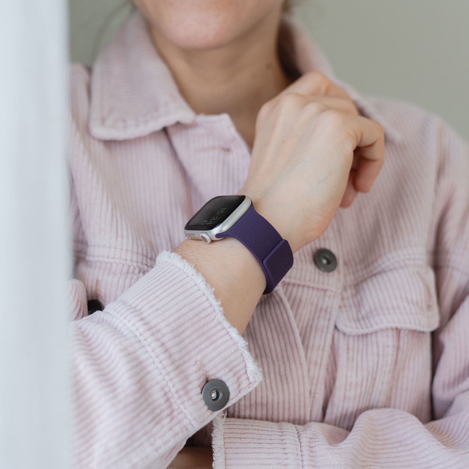 Person trägt eine lavendelfarbene Cordjacke und eine Apple Watch mit dem Arktisband "Flexy" - ein magnetisches Silikonarmband in Lila der Marke arktisband -, die Hand nahe am Gesicht.