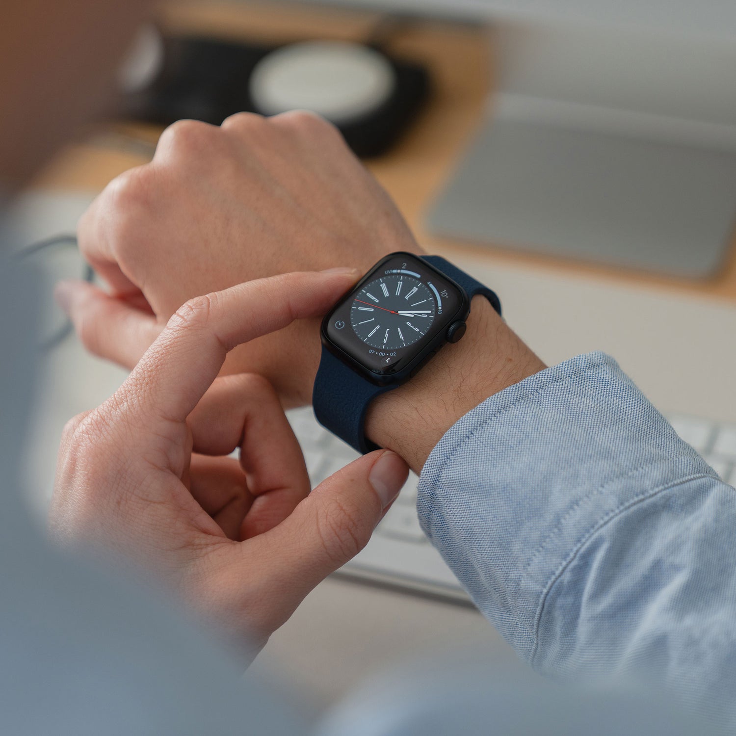 Eine Person, die das arktisband Apple Watch magnetisches Silikonarmband "Flexy" von arktisband in blau trägt, tippt auf den Bildschirm ihrer Smartwatch, während sie an einem Schreibtisch sitzt und eine Tastatur in der Nähe hat.