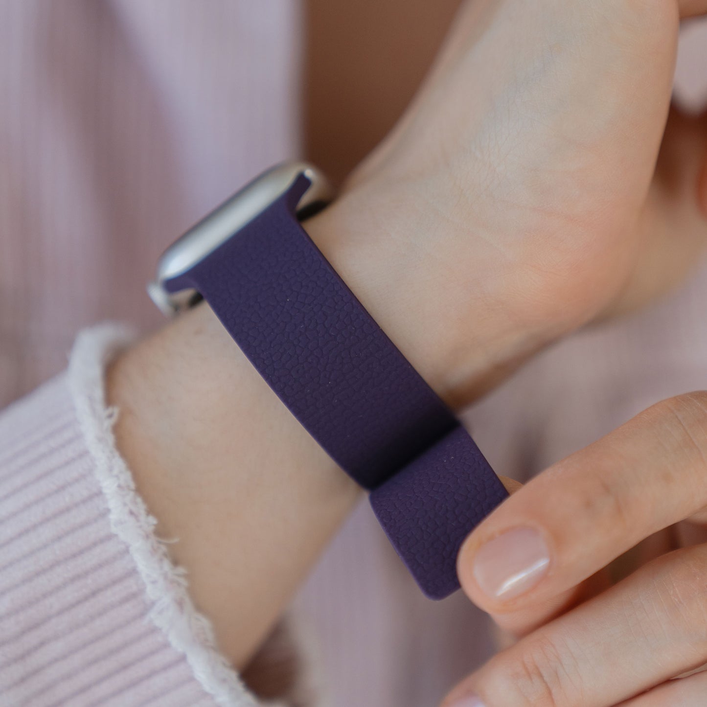 Nahaufnahme einer Person, die ein Arktisband Apple Watch magnetisches Silikonarmband "Flexy" in Lila an ihrem Handgelenk anpasst.