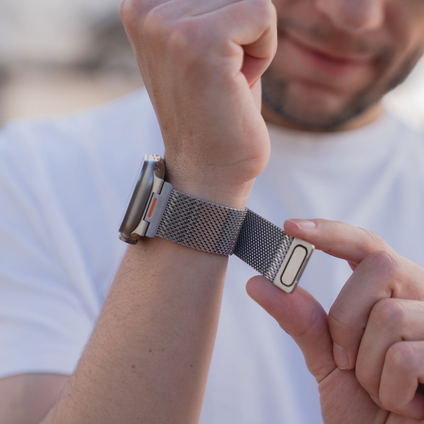 Eine Person befestigt ein arktisband Apple Watch Milanaise Armband "Bold SE" von arktisband an ihrer Apple Watch und trägt dabei ein weißes Hemd.