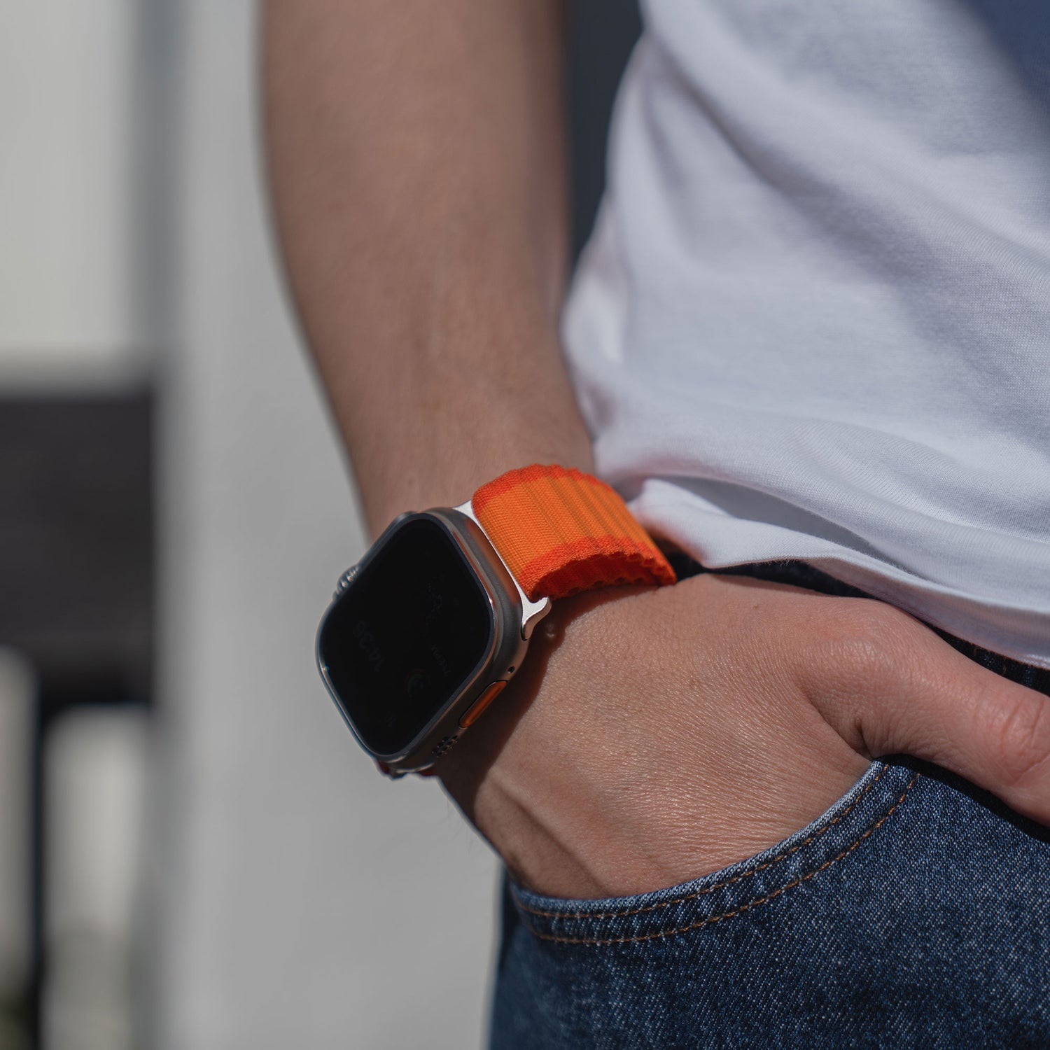 Eine Person, die ein arktisband Apple Watch Armband "CoreX" mit einem orangefarbenen Band trägt, die Hand in der Tasche, bekleidet mit Jeans und einem weißen Hemd.