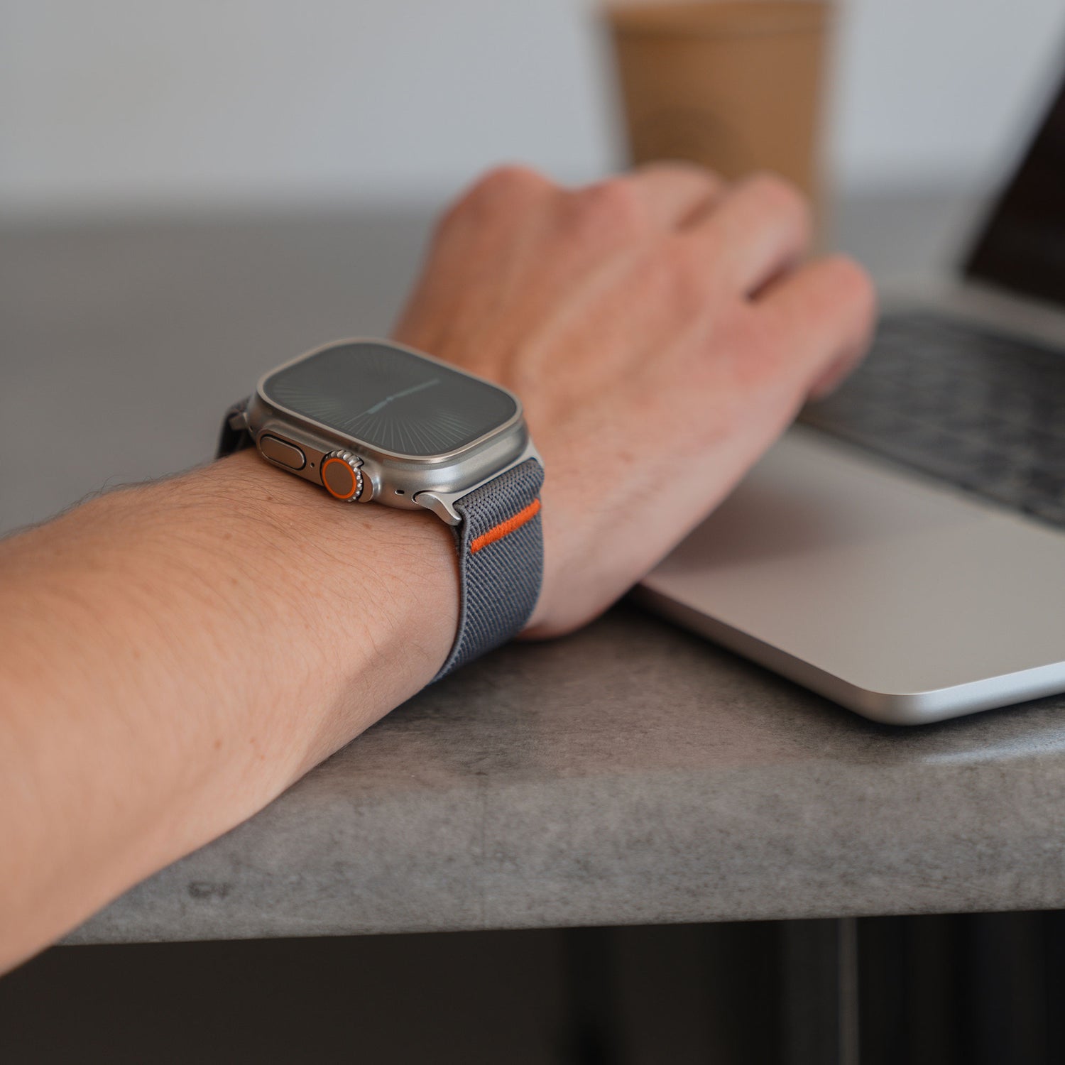 Jemand, der ein Arktisband Apple Watch Nylonarmband "FlexOne" trägt, benutzt einen Laptop an einem Tisch mit einer Kaffeetasse im Hintergrund.