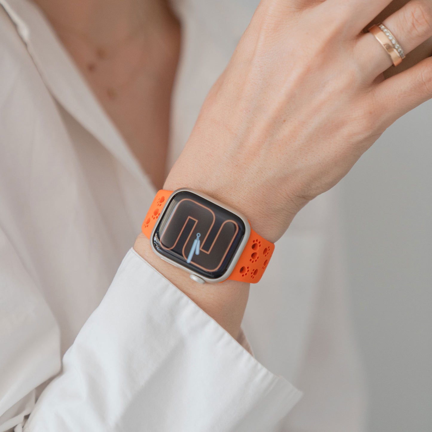 Eine Person, die das arktisband Apple Watch Silikonarmband "Paw" von arktisband mit einem orangefarbenen Band und geometrischem Zifferblatt trägt, bekleidet mit einem weißen Hemd.