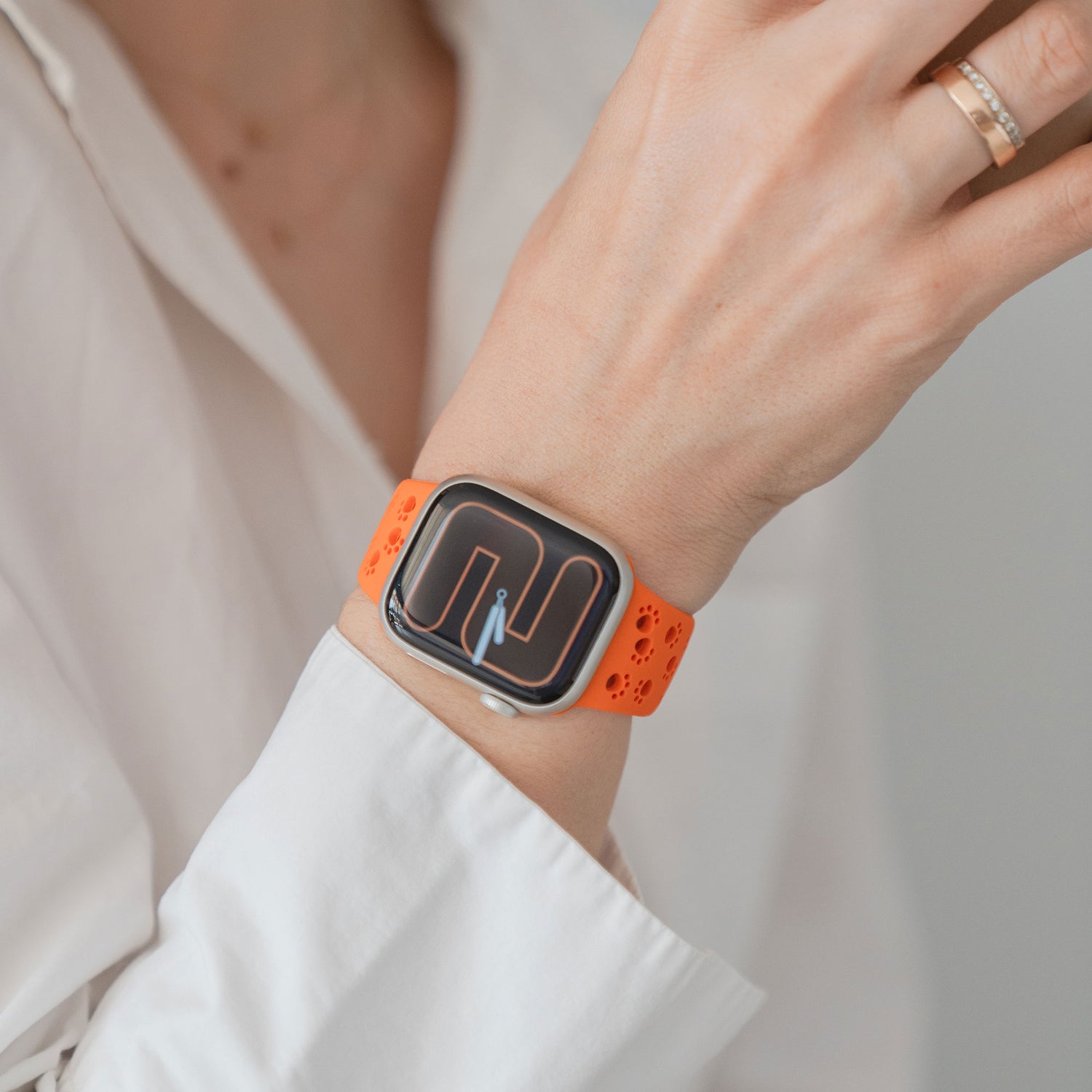 Eine Person, die das arktisband Apple Watch Silikonarmband "Paw" von arktisband mit einem orangefarbenen Band und geometrischem Zifferblatt trägt, bekleidet mit einem weißen Hemd.