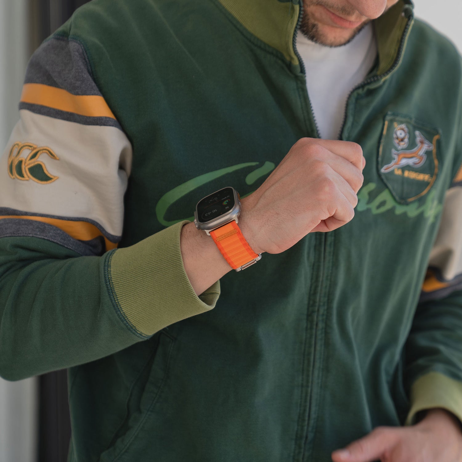 Eine Person in grüner Jacke blickt auf ihr Handgelenk und präsentiert sich stilecht im Wave-Look mit dem orangefarbenen arktisband Apple Watch Armband "CoreX" von arktisband.