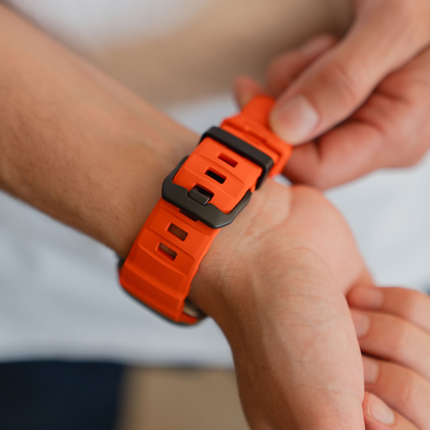 Jemand legt sich das arktisband Apple Watch Armband "Flux" in orange FKM mit einer Edelstahl Schließe um sein Handgelenk.