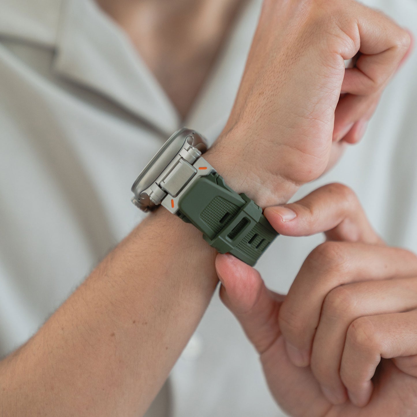 Eine Person passt ein grünes arktisband Apple Watch Ultra Armband „Atlas“ von arktisband an ihrem linken Handgelenk an, kombiniert mit einem hellen Hemd.