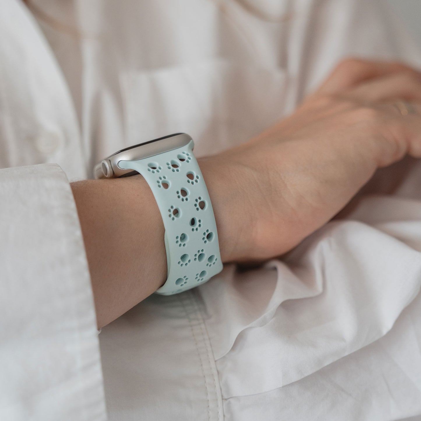 Nahaufnahme einer Apple Watch mit dem Arktisband "Paw" Silikonarmband in Hellblau mit Pfotenabdrücken am Handgelenk einer Person.