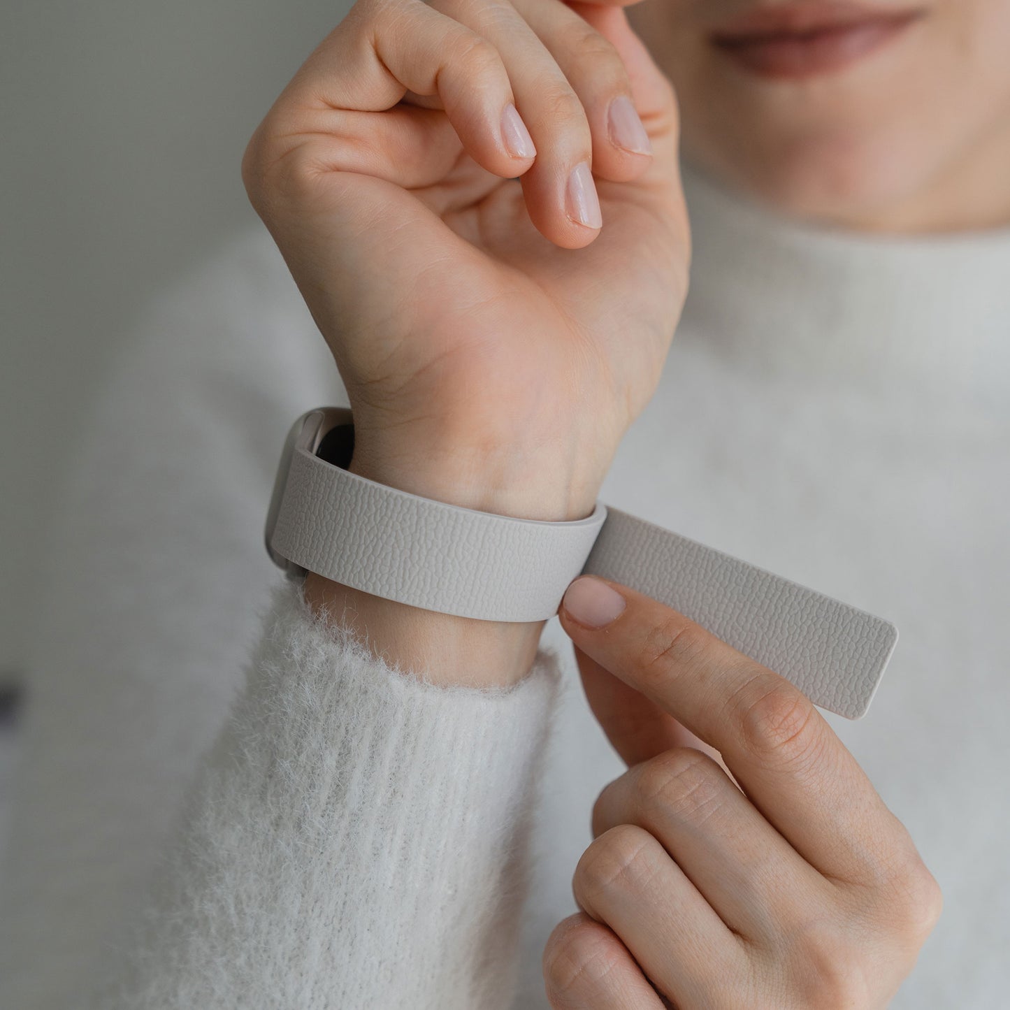 Eine Person befestigt das Arktisband Apple Watch magnetisches Silikonarmband "Flexy" in Hellgrau an ihrem linken Handgelenk und trägt einen weißen flauschigen Pullover.