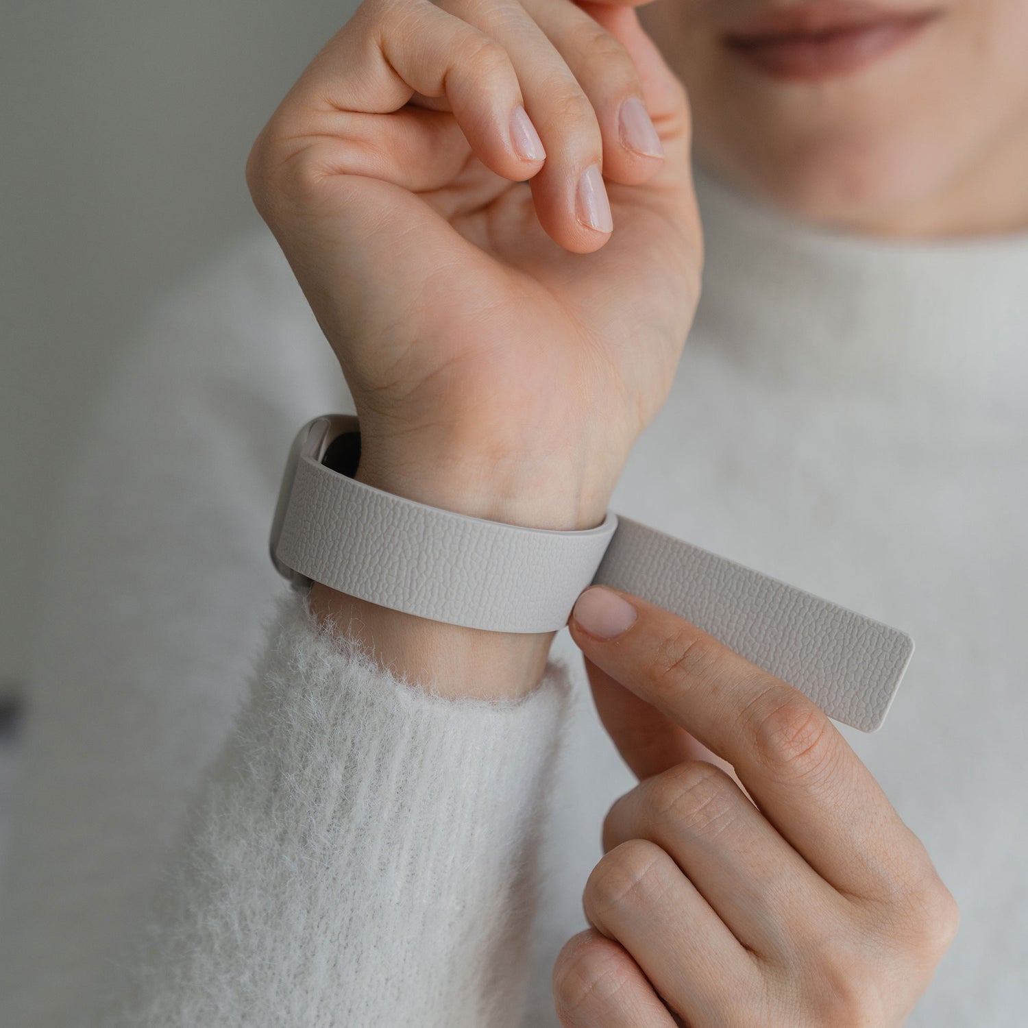 Eine Person befestigt das Arktisband Apple Watch magnetisches Silikonarmband "Flexy" in Hellgrau an ihrem linken Handgelenk und trägt einen weißen flauschigen Pullover.