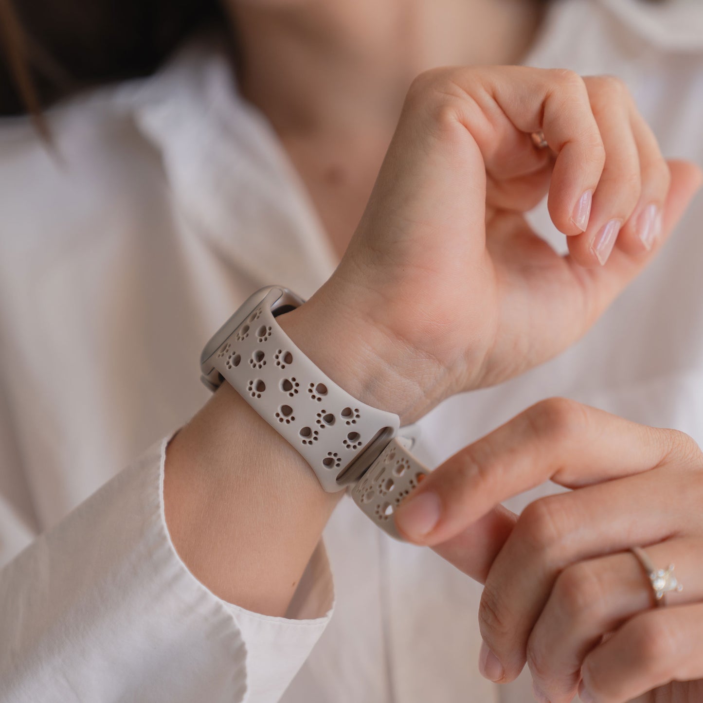 Jemand befestigt das arktisband Apple Watch Silikonarmband "Paw", ein weißes Armband mit Tatzenmotiv von arktisband, an seinem Handgelenk.