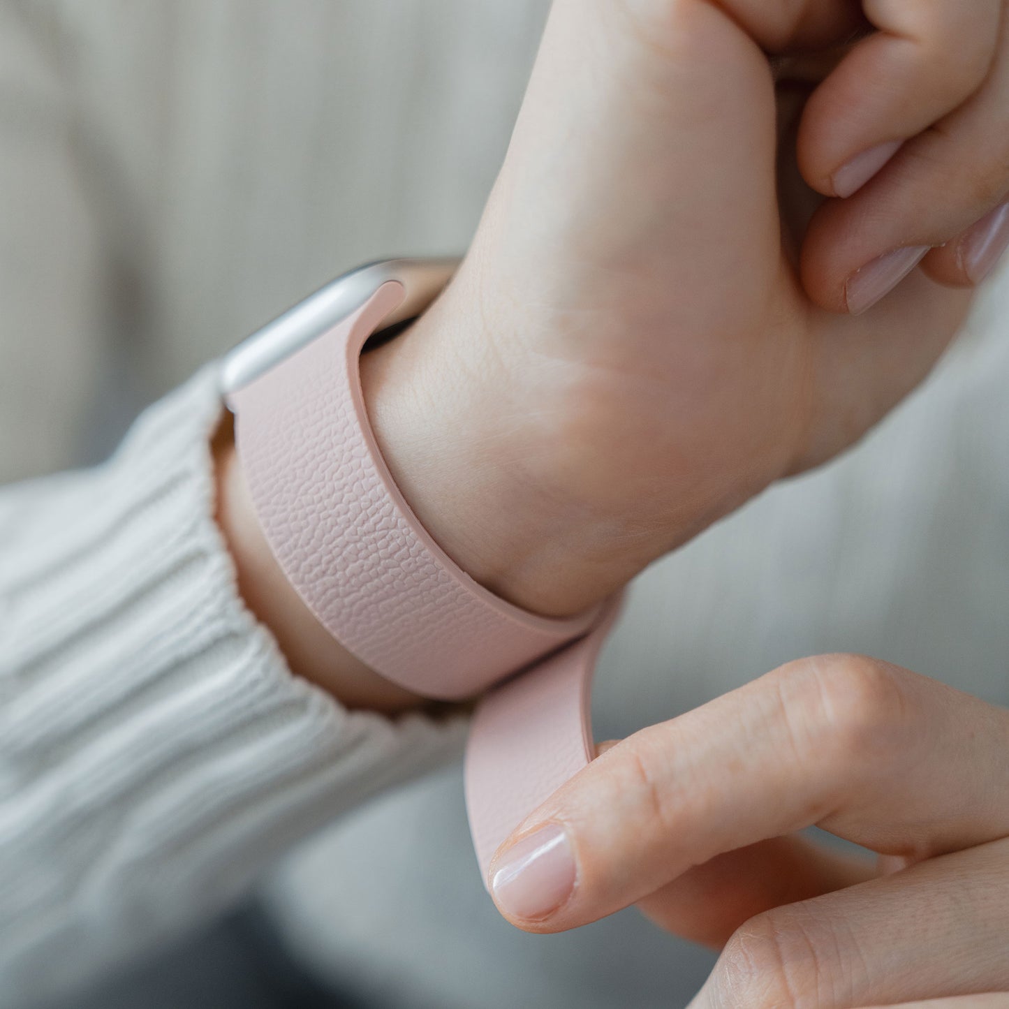 Jemand legt sich das magnetische Apple Watch Silikonarmband "Flexy" in Pink um das Handgelenk und kombiniert es mit einem leichten Strickpullover - ein modisches Must-have für jeden Apple Watch Armband Fan.