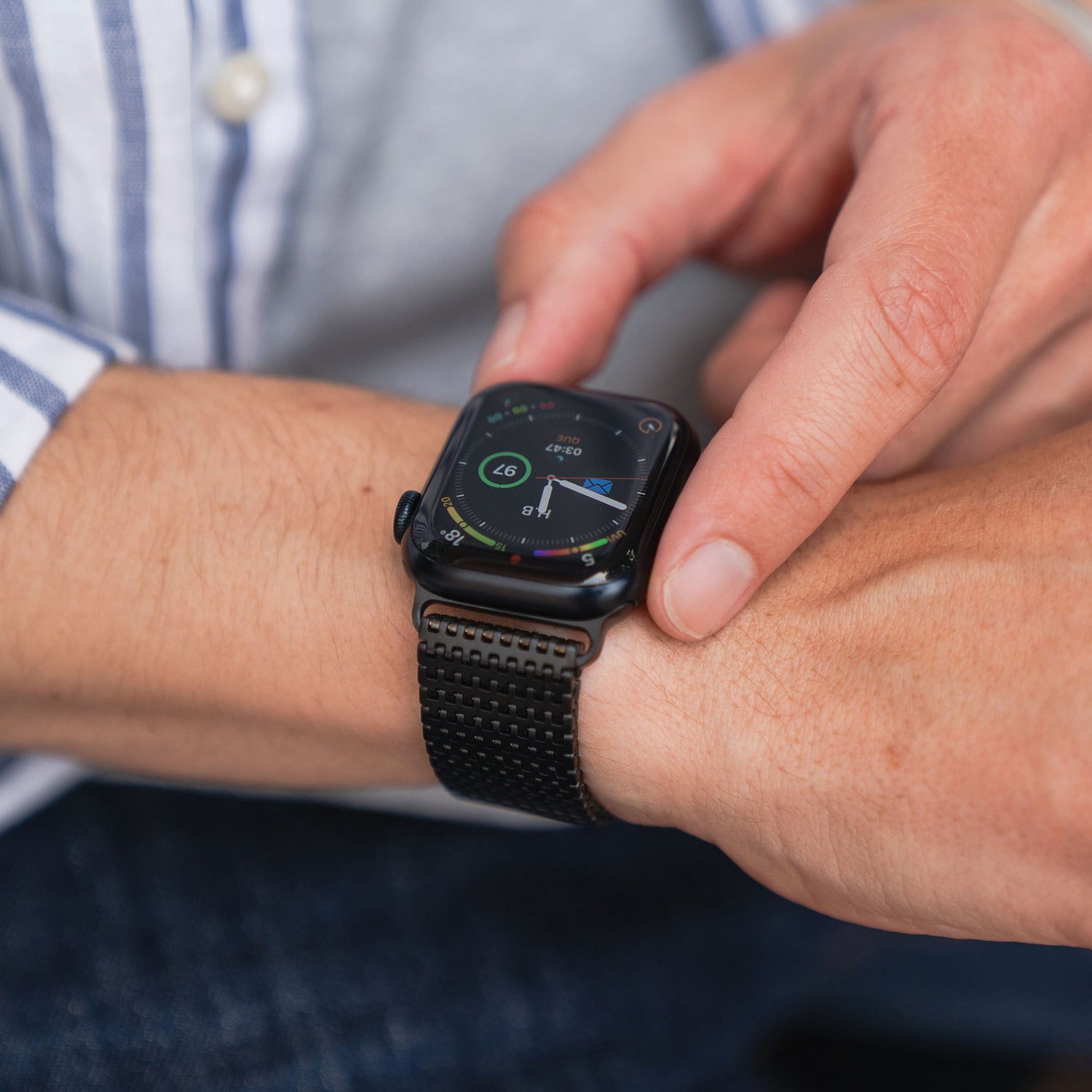 Eine Person im gestreiften Hemd checkt ihre Apple Watch, die mit dem arktisband Aurora Edelstahl Armband von arktisband ausgestattet ist.