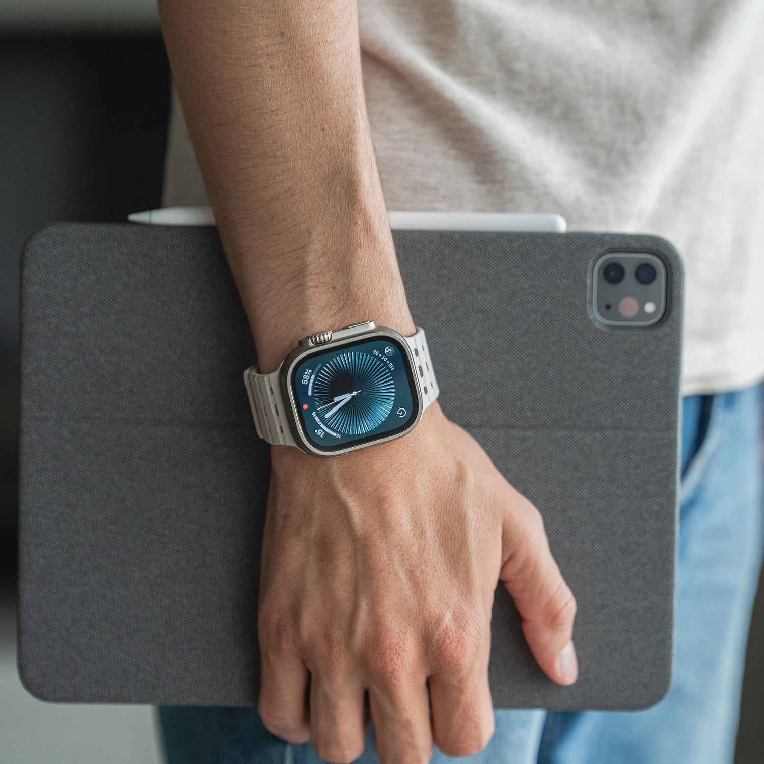 Eine Person, die das magnetische Silikonarmband „Power“ von arktis für die Apple Watch trägt, hält ein graues Tablet mit Stift in der Hand. Nur Oberkörper und Hand sind zu sehen, bekleidet mit einem hellen Hemd und Jeans.