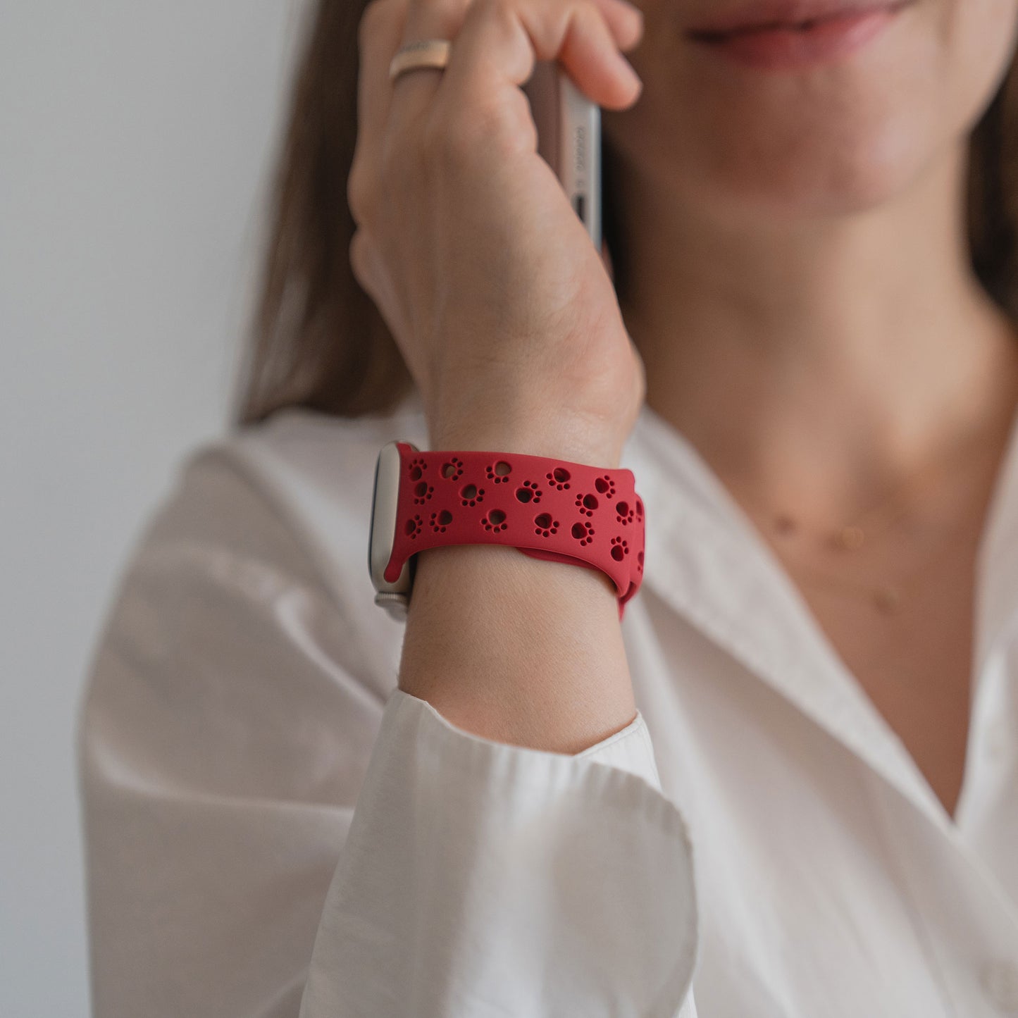 Frau in weißem Hemd telefoniert, trägt ein Arktisband Apple Watch Silikonarmband "Paw" mit Pfotenmotiv-Ausschnitten.