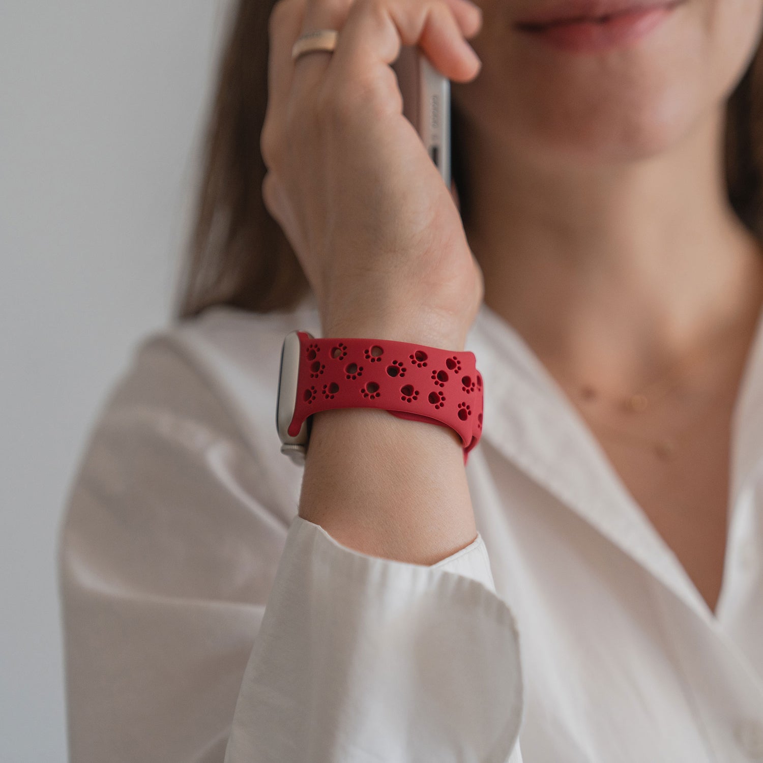 Frau in weißem Hemd telefoniert, trägt ein Arktisband Apple Watch Silikonarmband "Paw" mit Pfotenmotiv-Ausschnitten.