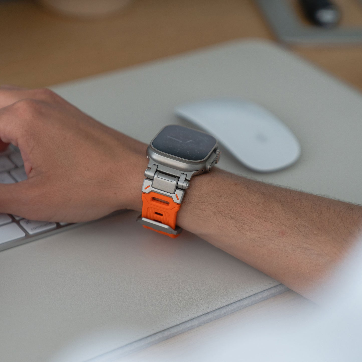 Eine Person, die das arktisband Apple Watch Ultra Armband „Atlas“ von arktisband mit Edelstahl-Elementen trägt, legt ihre linke Hand auf eine Tastatur, im Hintergrund sind eine weiße Maus und eine Schreibtischoberfläche zu sehen.