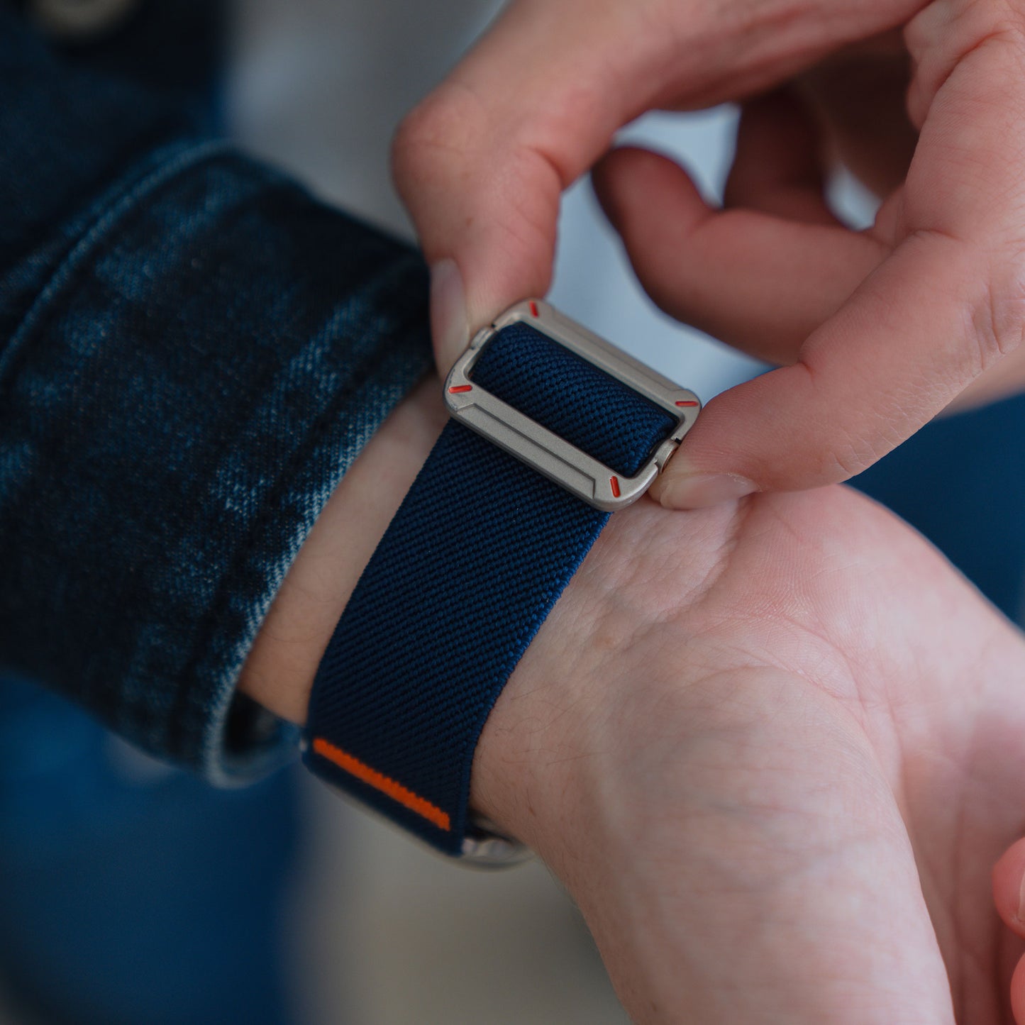 Eine Person befestigt ein arktisband Apple Watch Nylonarmband "FlexOne" (blau, silberne Schnalle) um ihr Handgelenk - ideal für ihre Apple Watch.