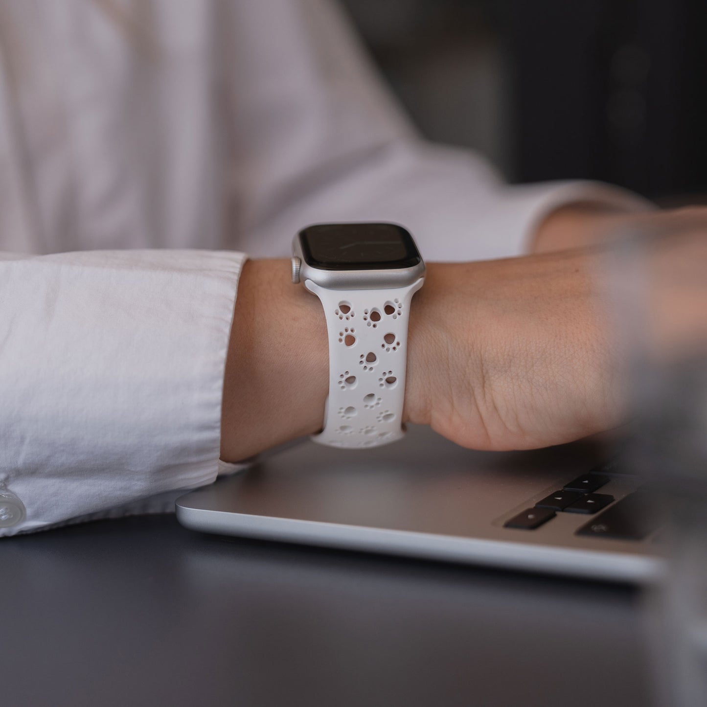 Eine Person in einem weißen Hemd tippt auf einem Laptop, während sie ein arktisband Apple Watch Silikonarmband "Paw" von arktisband trägt.