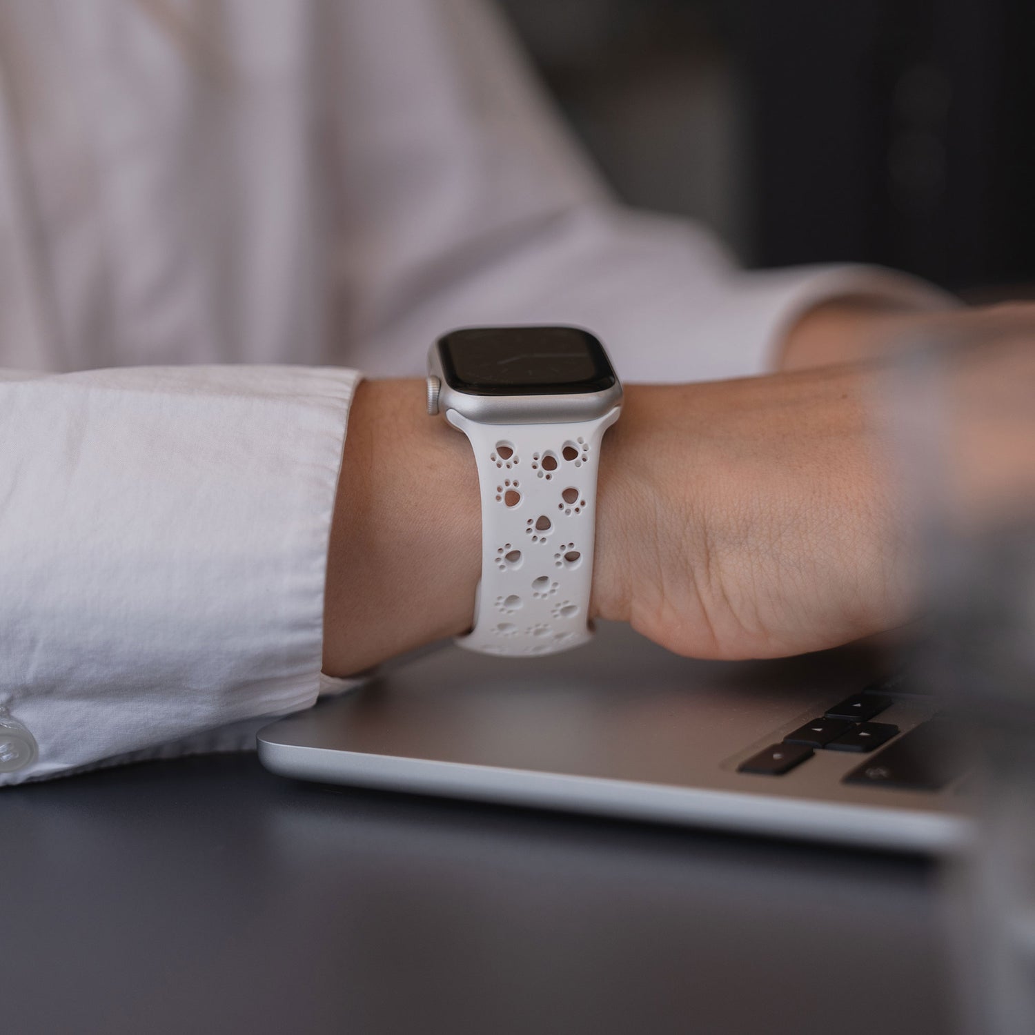 Eine Person in einem weißen Hemd tippt auf einem Laptop, während sie ein arktisband Apple Watch Silikonarmband "Paw" von arktisband trägt.