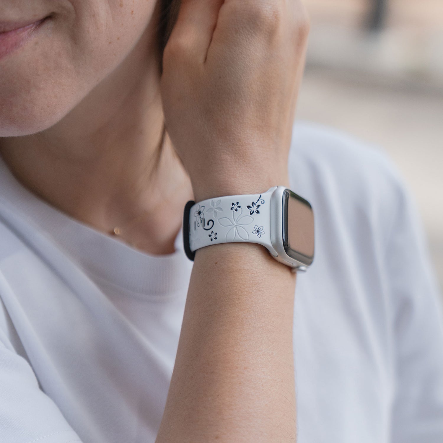 Eine Person trägt eine weiße Smartwatch mit dem Arktisband Apple Watch Silikonarmband "Bloom" mit einem floralen Muster am Handgelenk.