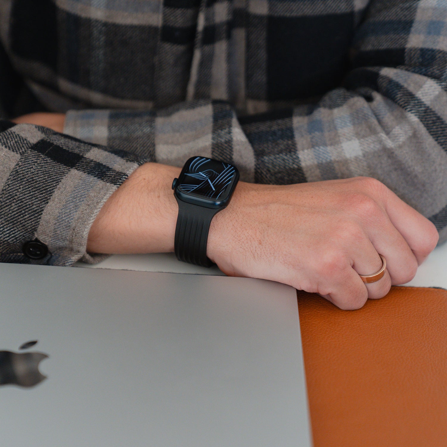 Eine Person, die ein kariertes Hemd und das arktisband Apple Watch Armband "Skandi" von arktisband trägt, stützt ihre Hand neben einem Laptop auf einem Schreibtisch ab.