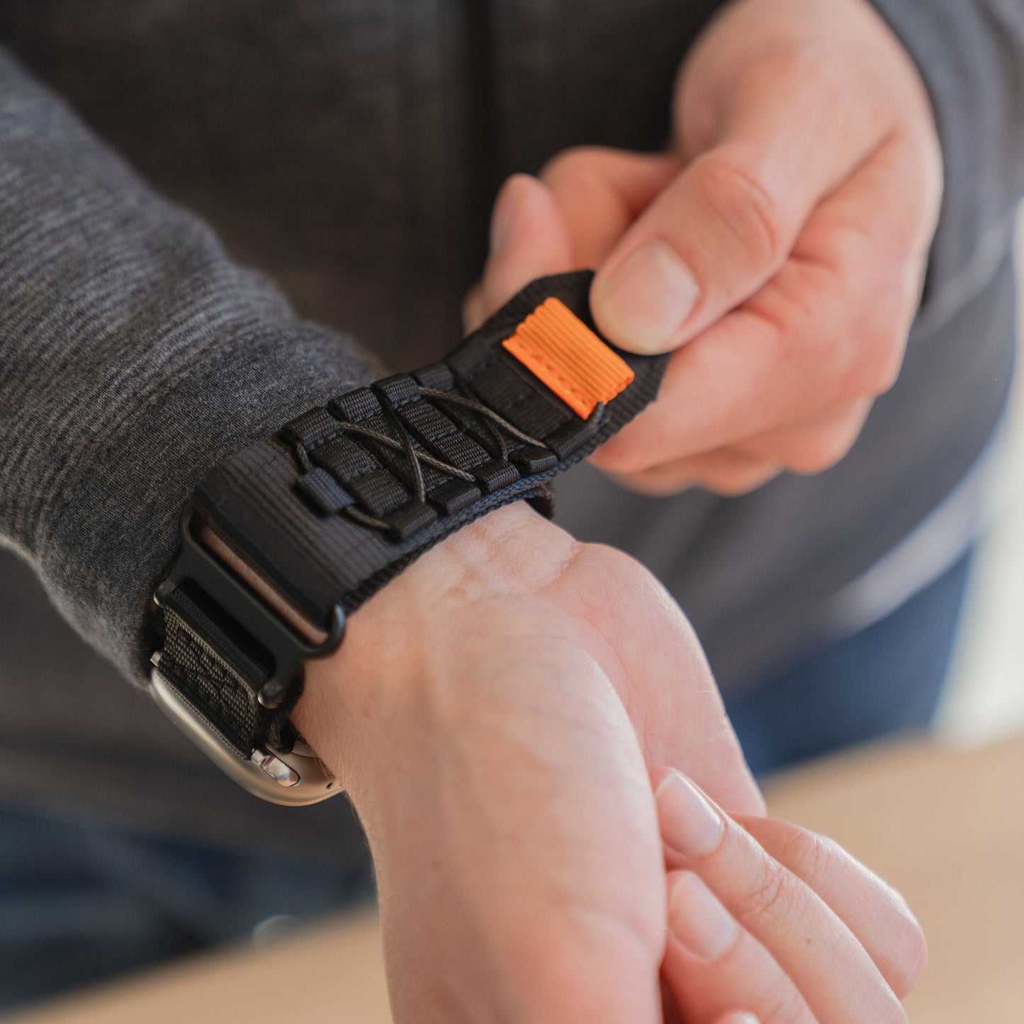 Jemand legt sich das arktisband Apple Watch Outdoor Armband "Forge" von arktisband mit schwarzem Band und orangefarbener Lasche um das Handgelenk.