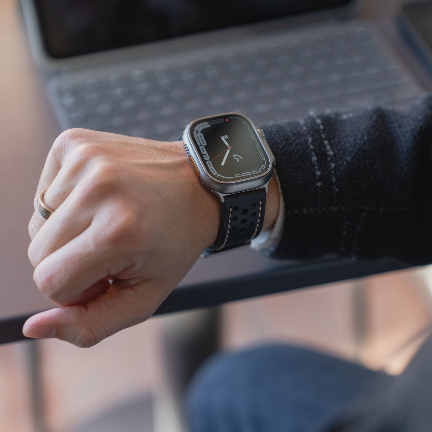 Eine Person, die ein Arktisband Apple Watch Lederarmband "Toronto" trägt, sitzt neben einem Tisch mit einem Laptop.
