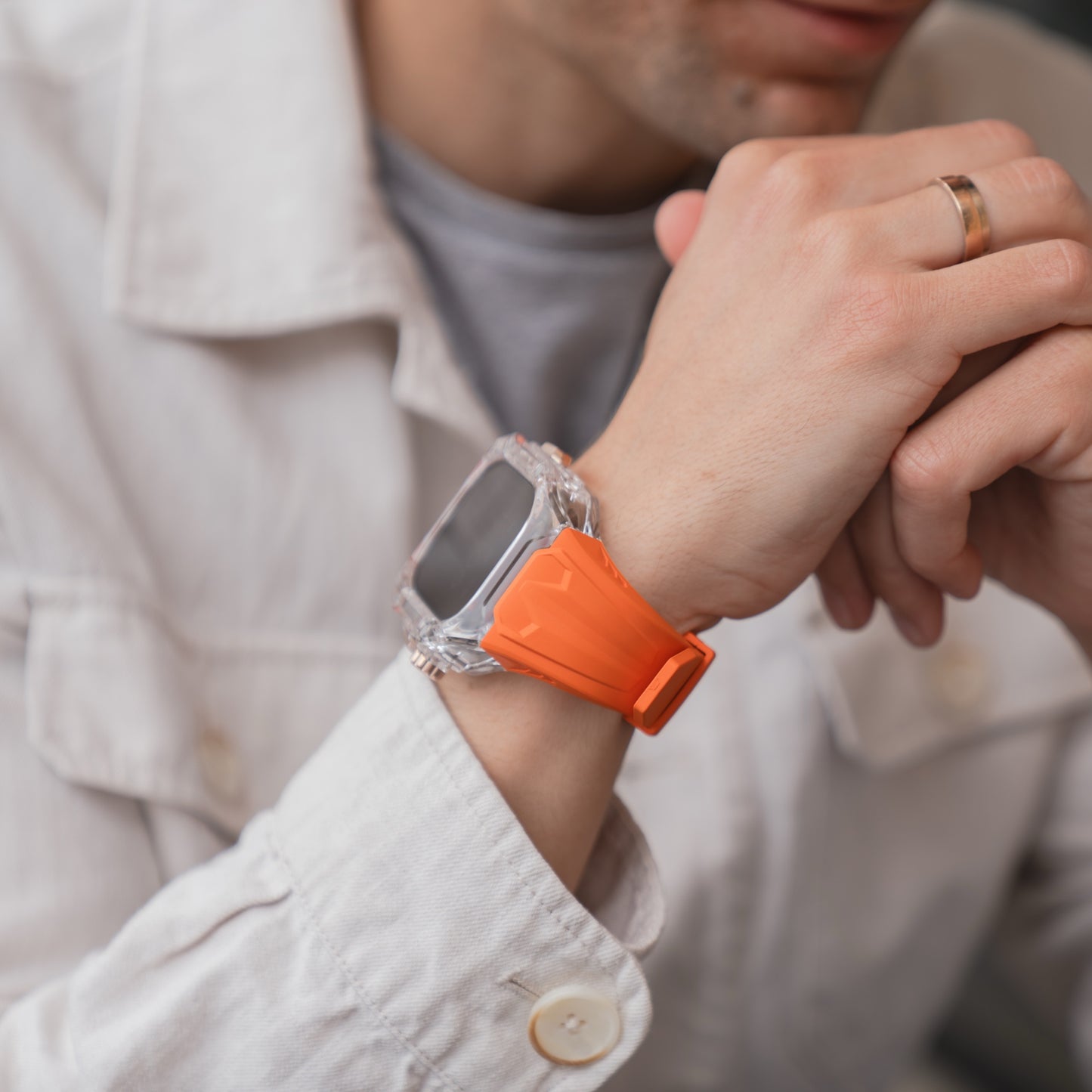 Person, die eine weiße Jacke und ein orangefarbenes arktisband Apple Watch Armband "Armor Fusion" von arktisband trägt und ihr Kinn auf die verschränkten Hände stützt.