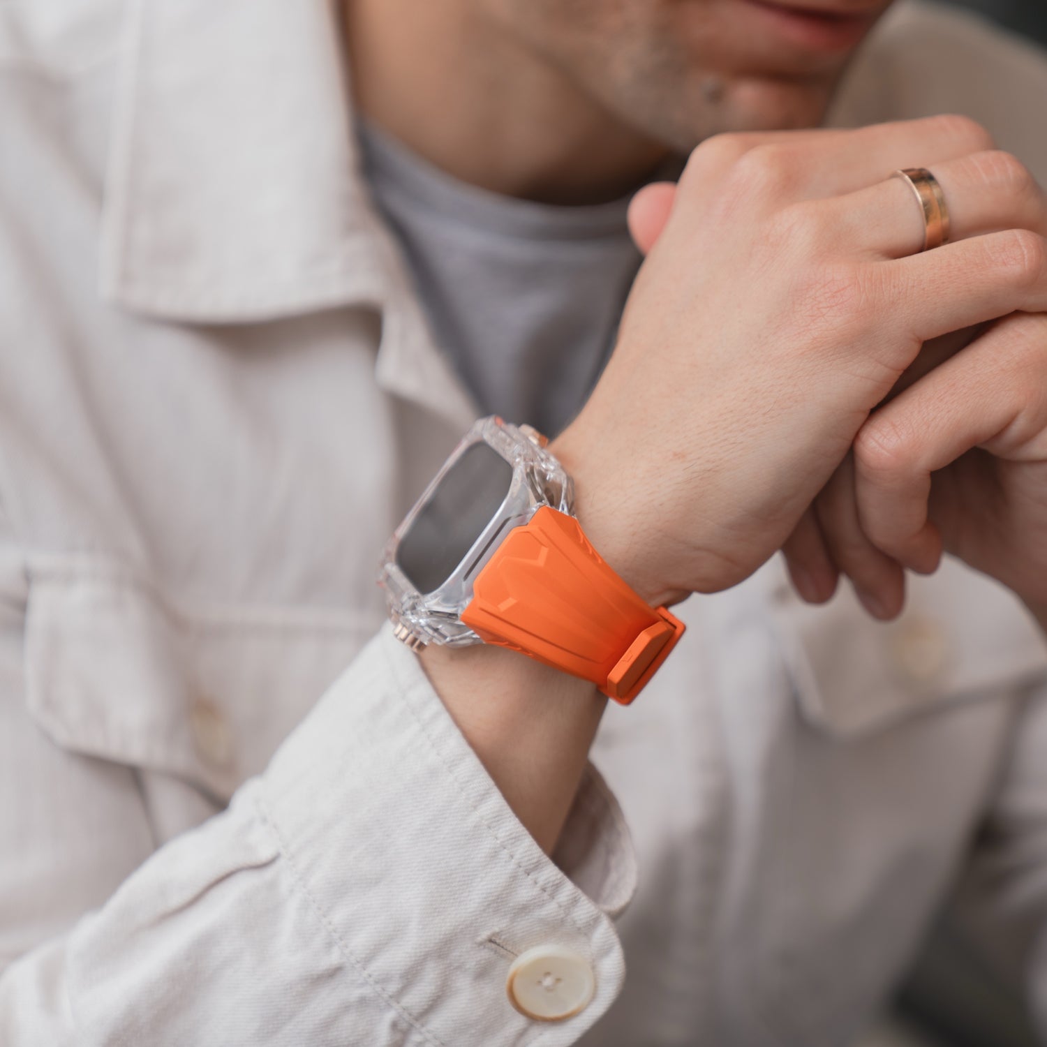 Person, die eine weiße Jacke und ein orangefarbenes arktisband Apple Watch Armband "Armor Fusion" von arktisband trägt und ihr Kinn auf die verschränkten Hände stützt.