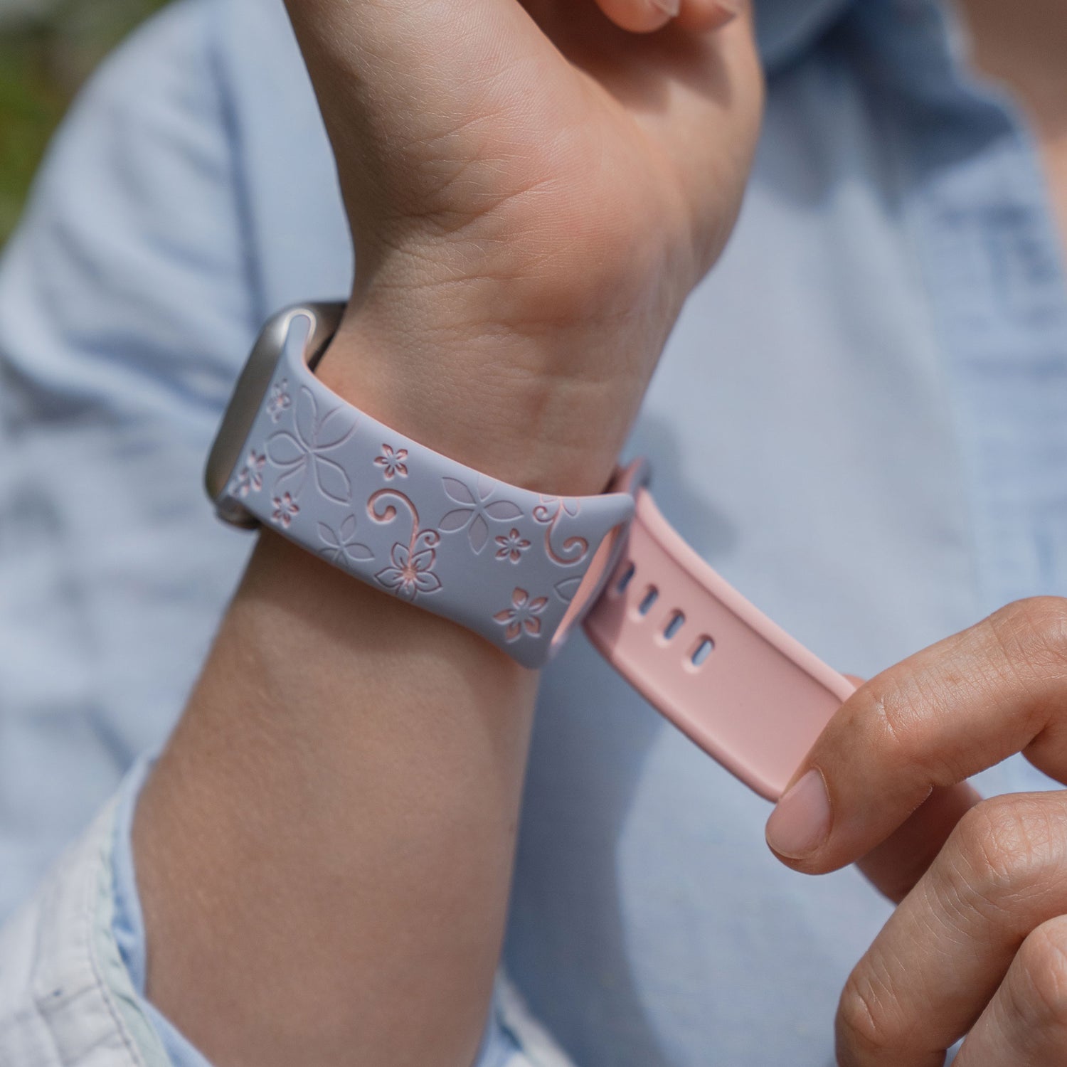 Eine Person befestigt das Arktisband Apple Watch Silikonarmband "Bloom" mit einem rosa Blumenmuster an ihrem Handgelenk.