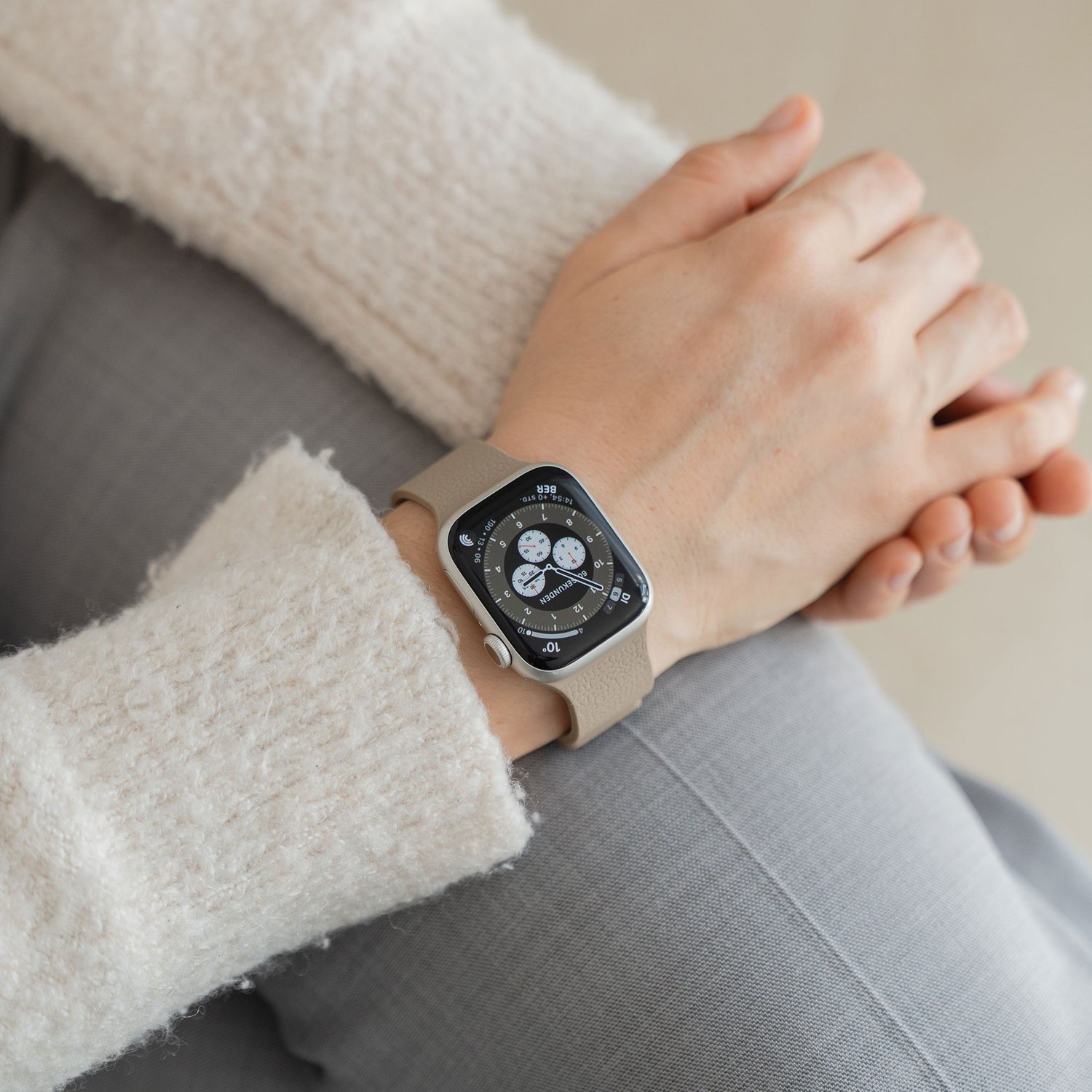 Eine Person, die eine Apple Watch mit digitaler Anzeige und dem beigen Arktisband Apple Watch magnetisches Silikonarmband "Flexy" trägt, legt die Hände auf den Schoß.