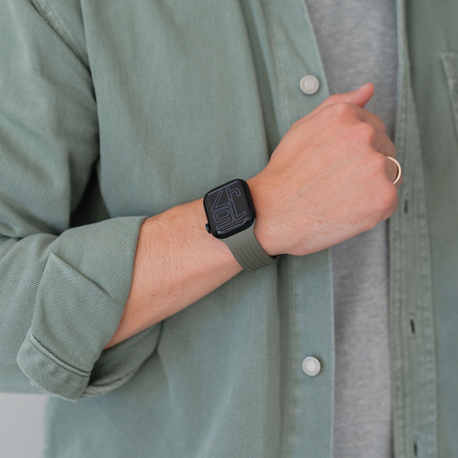 Eine Person trägt ein arktisband Apple Watch Armband "Skandi" von arktisband in grün und ein dazu passendes grünes Hemd, das ihr linkes Handgelenk und ihre Hand mit einem Ring zeigt.