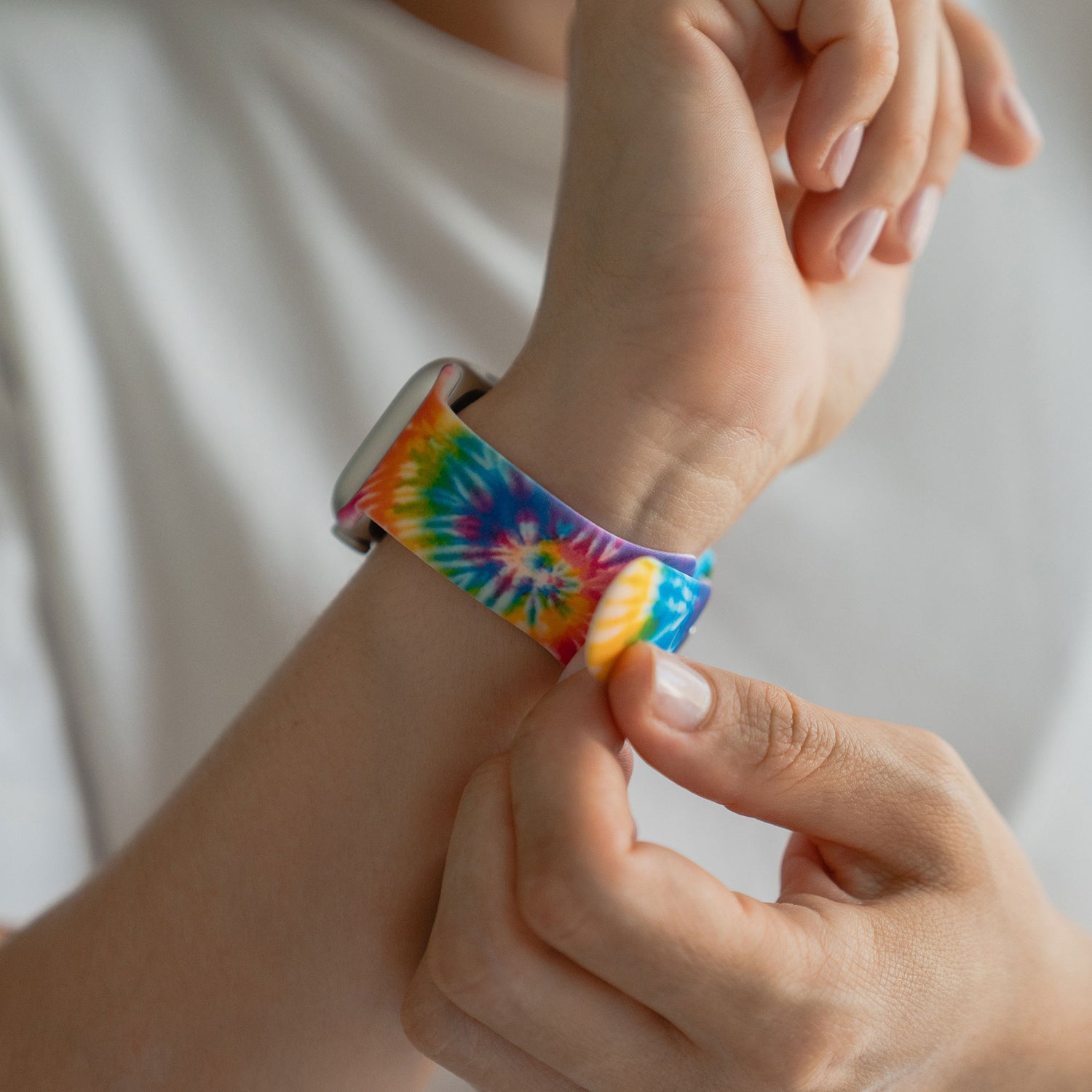 Jemand legt sich ein arktisband Batik Rainbow Apple Watch Armband von arktisband mit einem bunten Batik-Design um das Handgelenk.