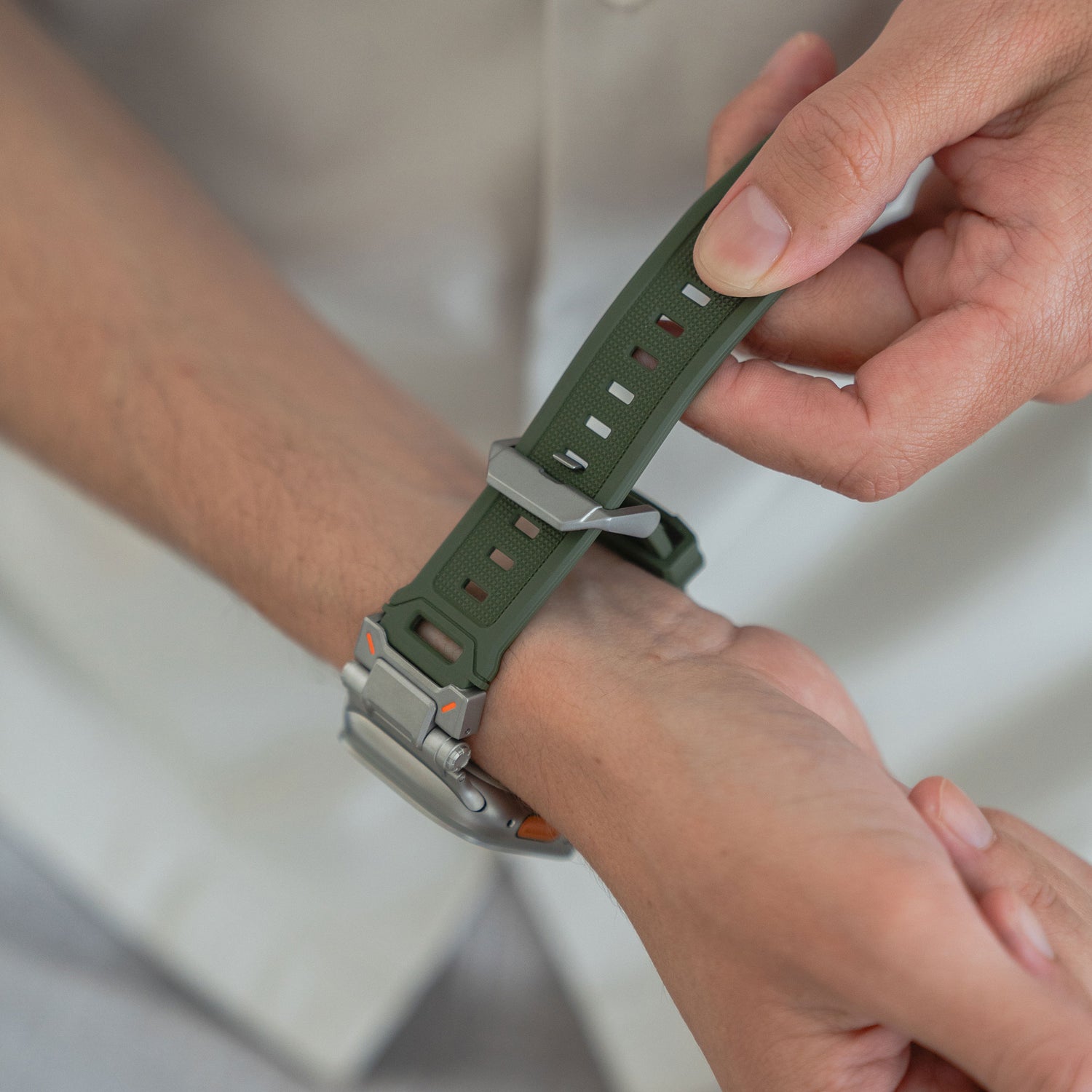 Man befestigt das grüne Arktisband Apple Watch Ultra Armband „Atlas“ mit robustem Design und TPU-Edelstahlelementen am Handgelenk.