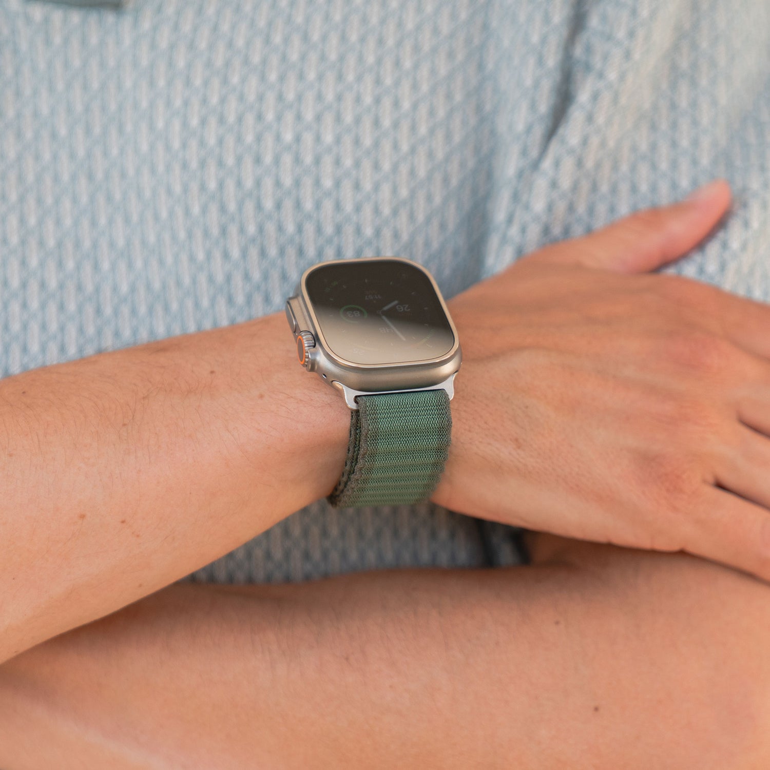 Der Träger des arktisband Apple Watch Nylonarmbands „Venture“ in Wave-Look Grün hat die Arme vor der Brust verschränkt und trägt dazu ein hellblaues gemustertes Shirt – ideal für Outdoor-Fans.
