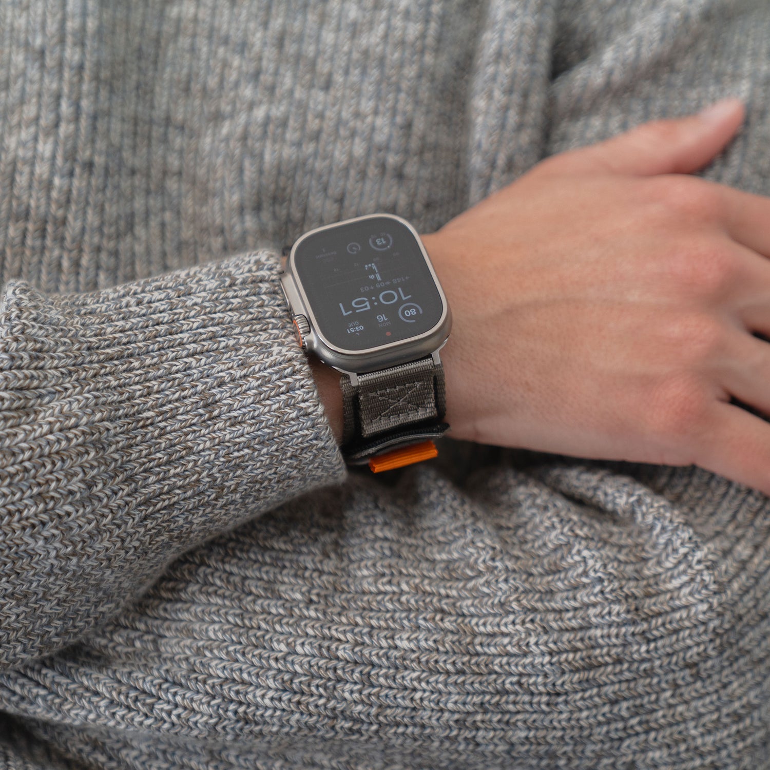 Jemand trägt das arktisband Apple Watch Outdoor Armband "Forge" von arktisband mit einem grauen Armband über dem Ärmel eines grauen Strickpullovers.