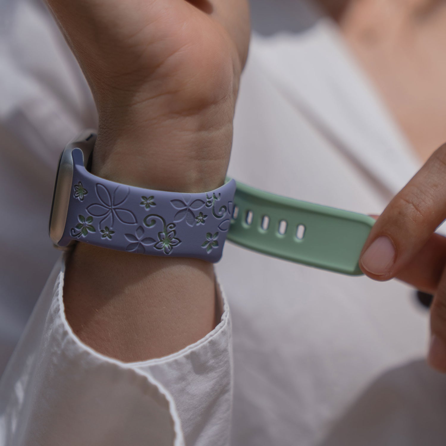 Nahaufnahme einer Person, die das arktisband Apple Watch Silikonarmband "Bloom" mit lila Blumenmuster und grünem Silikonband von arktisband befestigt.