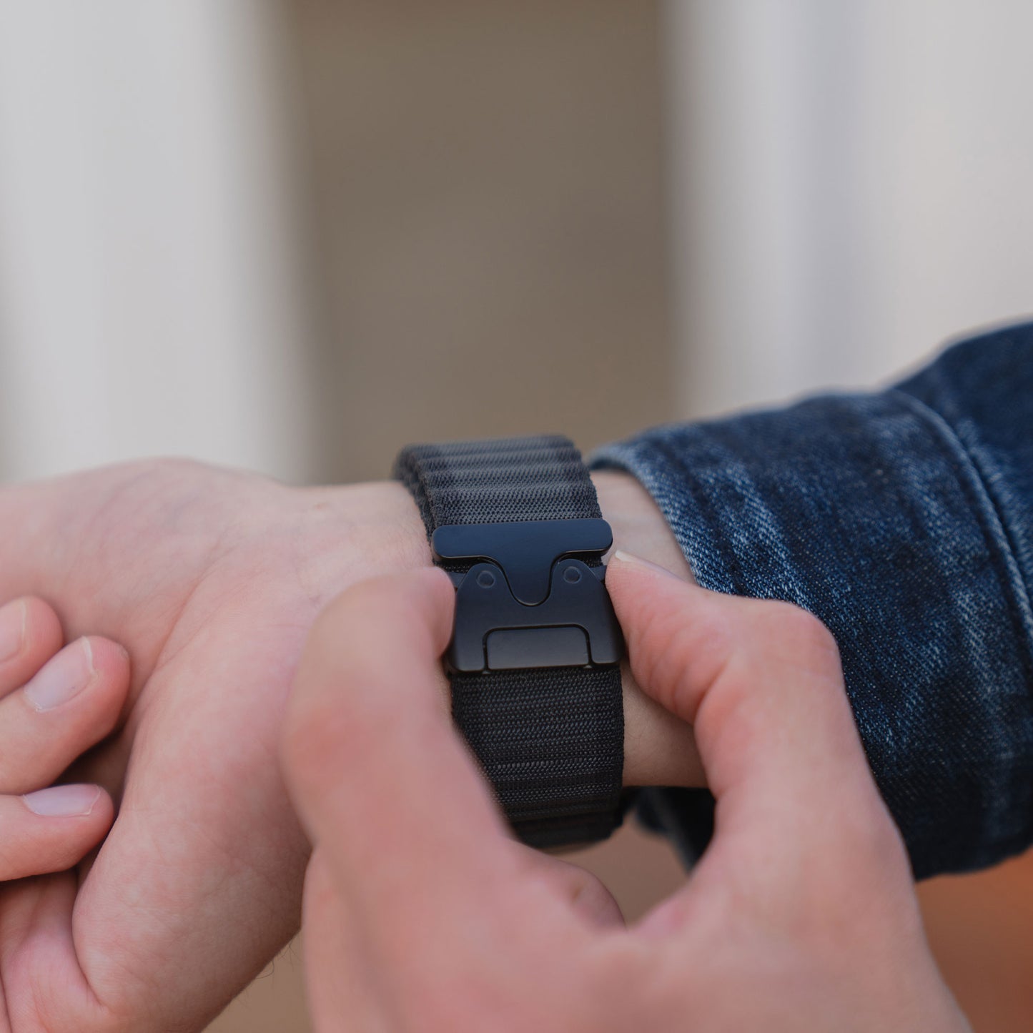 Eine Person, die ein Apple Watch Armband "CoreX" mit Parachute-Verschluss an ihrem Handgelenk befestigt und eine Jeansjacke trägt.