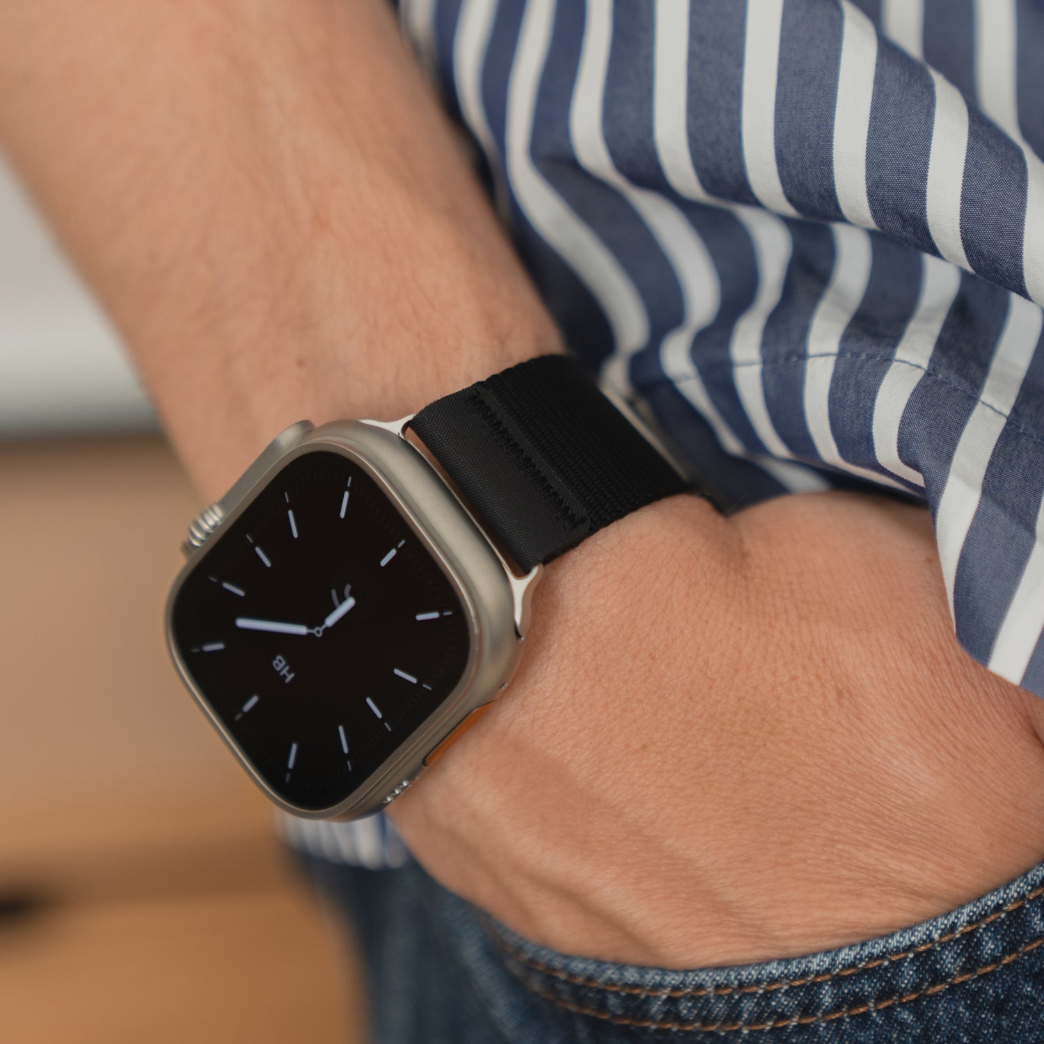 Eine Person trägt ein arktisband Apple Watch Armband "Terra" von arktisband mit einem extra breiten 24 mm Nylonband und ein gestreiftes Hemd, die Hand in der Jeanstasche.