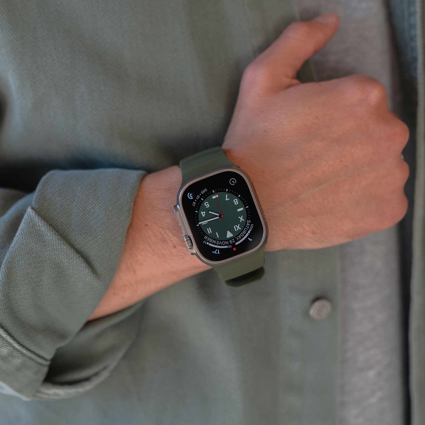 Eine Person trägt ein arktisband Apple Watch Armband "Flux" mit Kompassgesicht, FKM-Band und Edelstahl-Schließe, gepaart mit einer grünen Jacke und grauem Hemd.